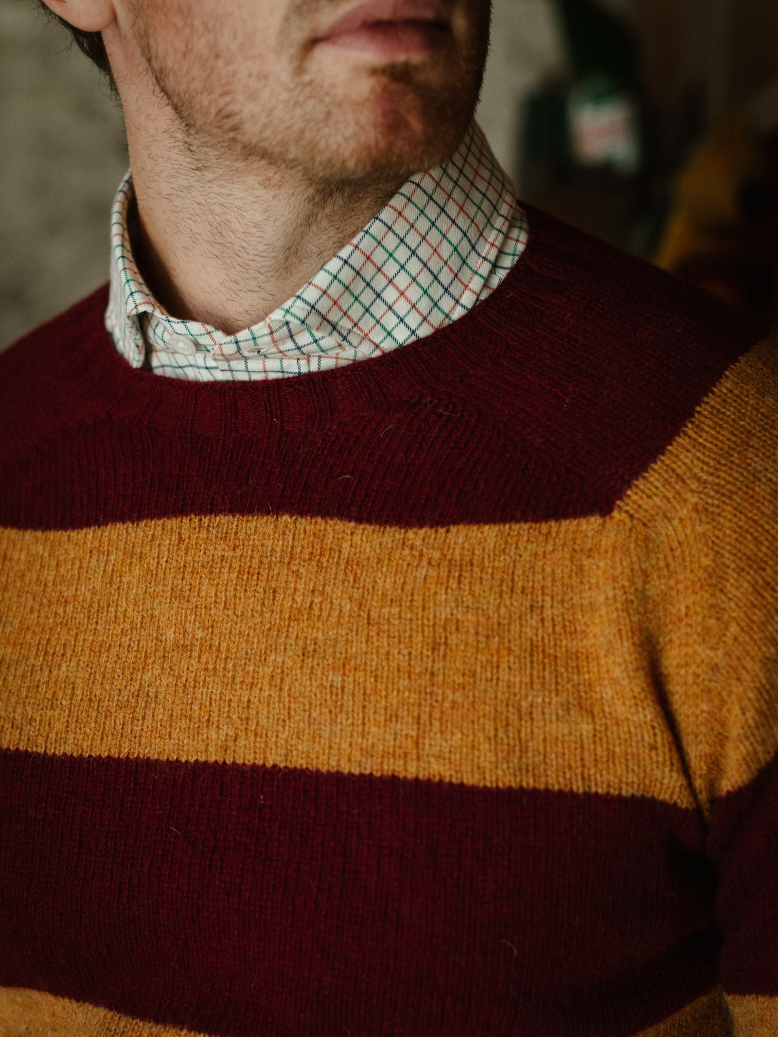 A person wears a Campbell's of Beauly Windowpane Shirt in white brushed cotton, layered under a burgundy and mustard yellow striped sweater. The image captures the lower half of the face and upper torso.