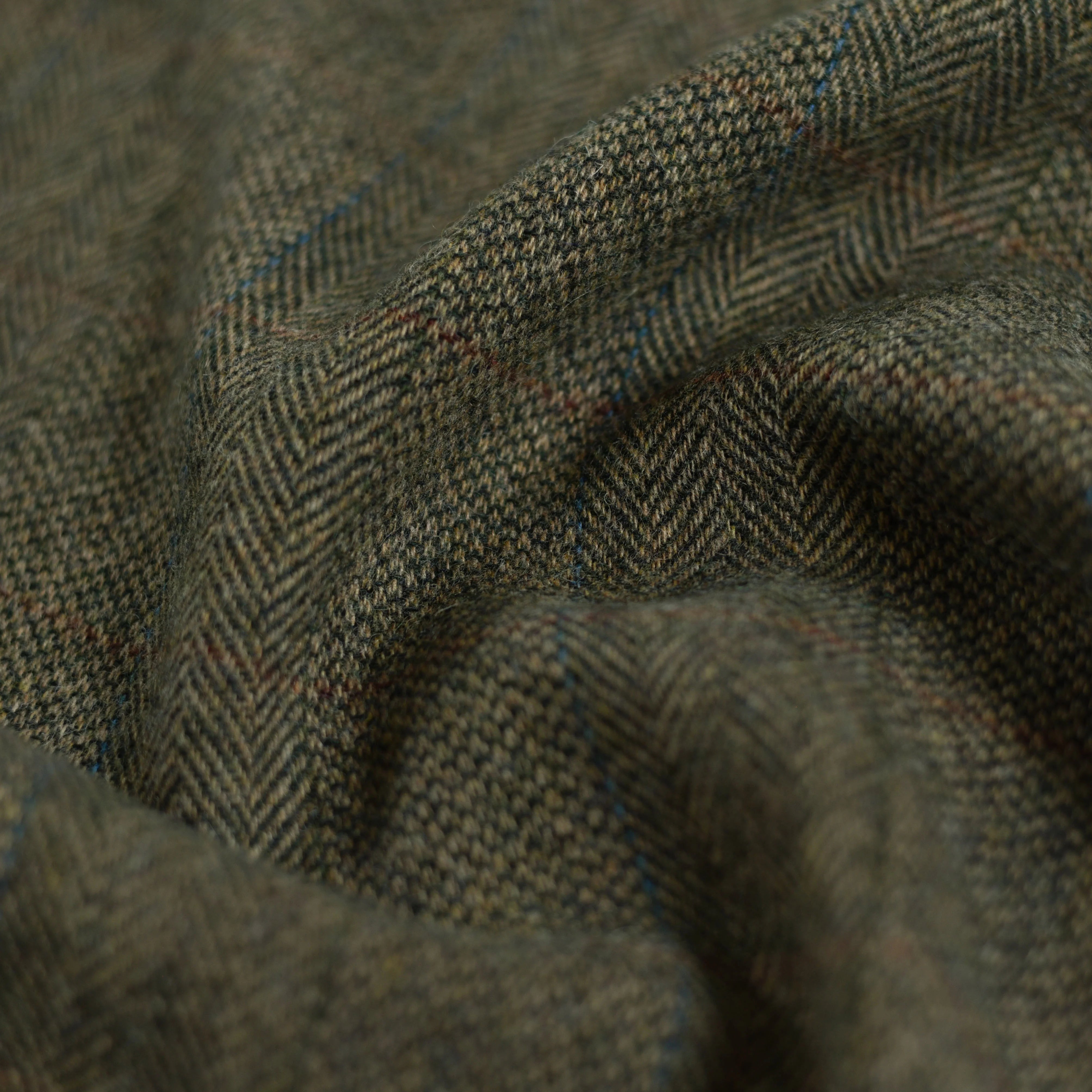 Close-up of Campbells of Beauly House Tweed 11059: green and brown herringbone Shetland wool with subtle blue and red stripes, highlighting the lightweight cloths texture, weave pattern, and gentle folds.