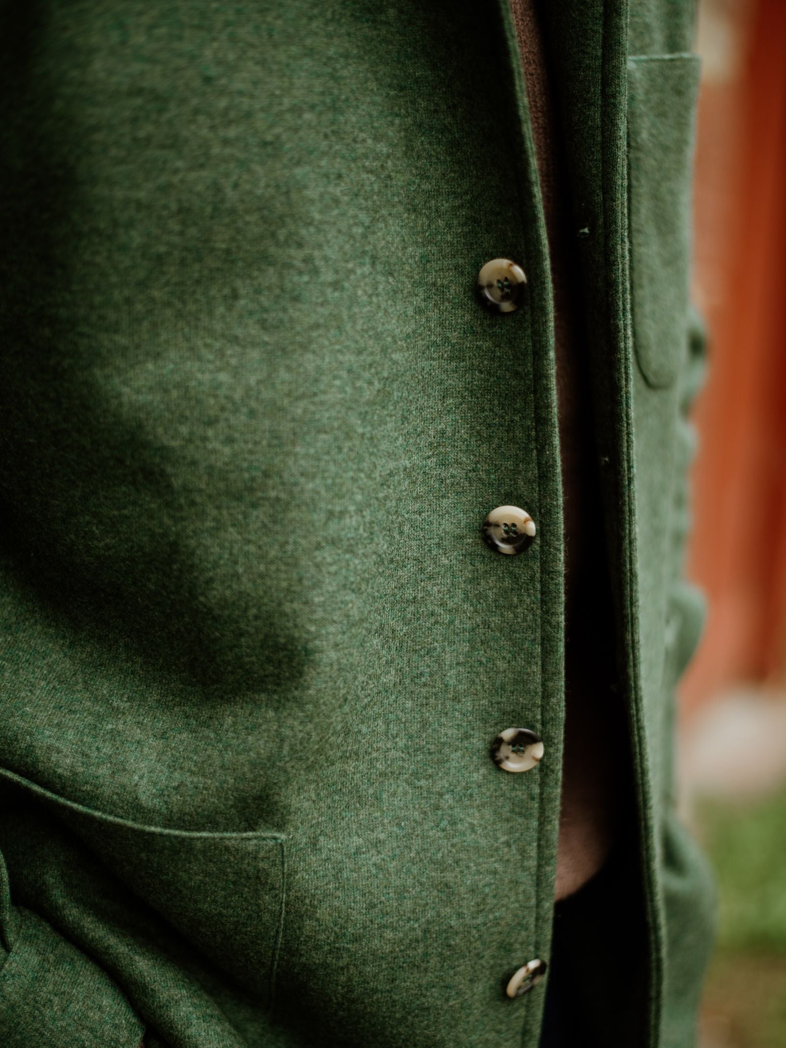 Close-up of a green Campbell's of Beauly Cashmere Teba Jacket shows four buttons and a pocket, highlighting fine texture and details, with the front side in focus—a testament to exceptional craftsmanship.