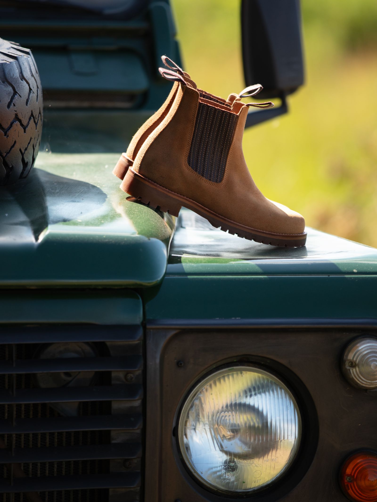 Campbell's of Beauly Leather Chelsea Boots in brown high-quality leather with elastic side panels rest on a green vehicle’s hood with a headlight and spare tire—an essential for any country wardrobe.