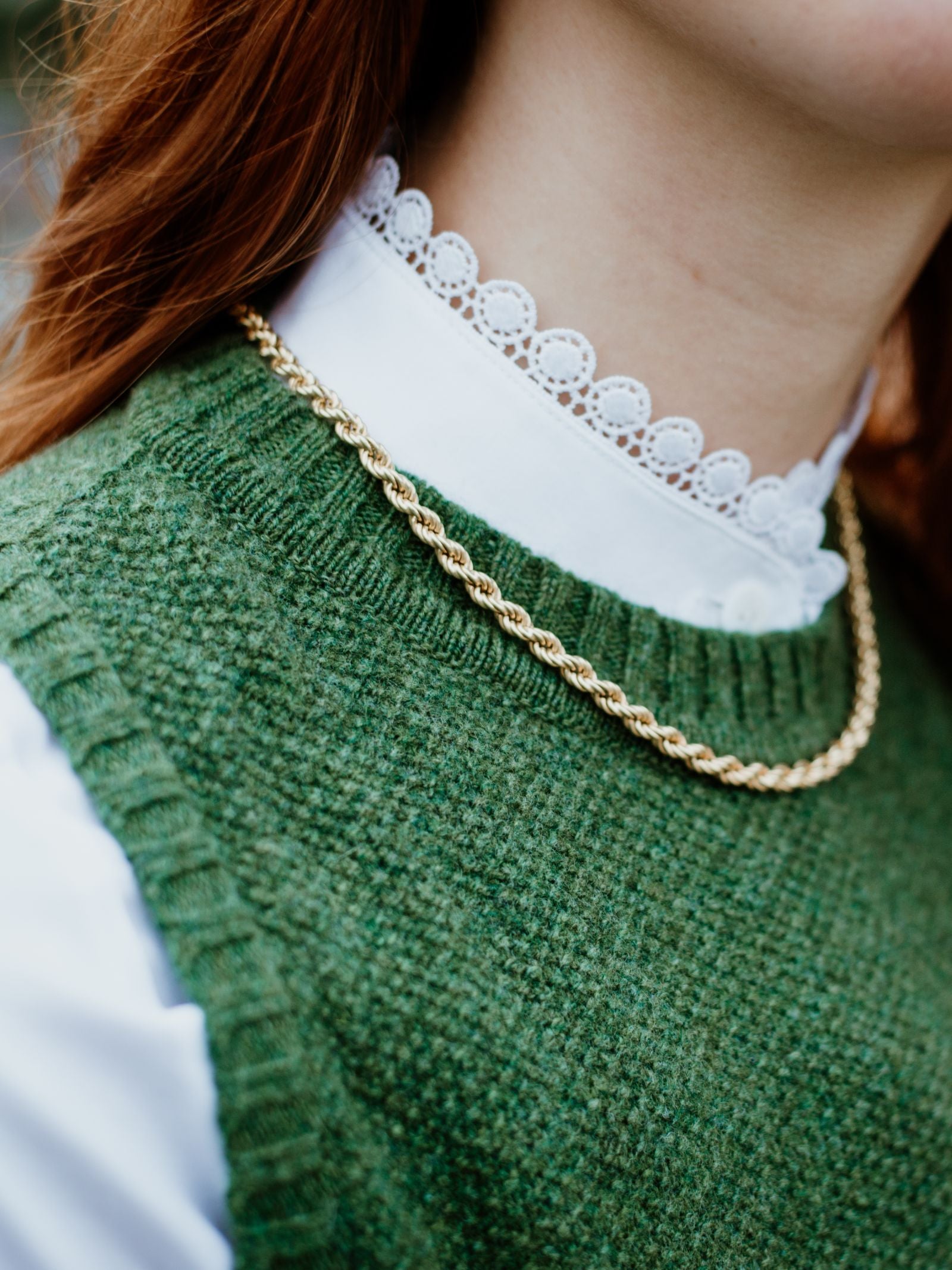 Close-up of a person wearing a white blouse with a scalloped lace collar, layered under the Campbells of Beauly Moss Stitch Crew Tank and accessorized with a gold rope chain; only the lower face, neck, and upper chest are visible.