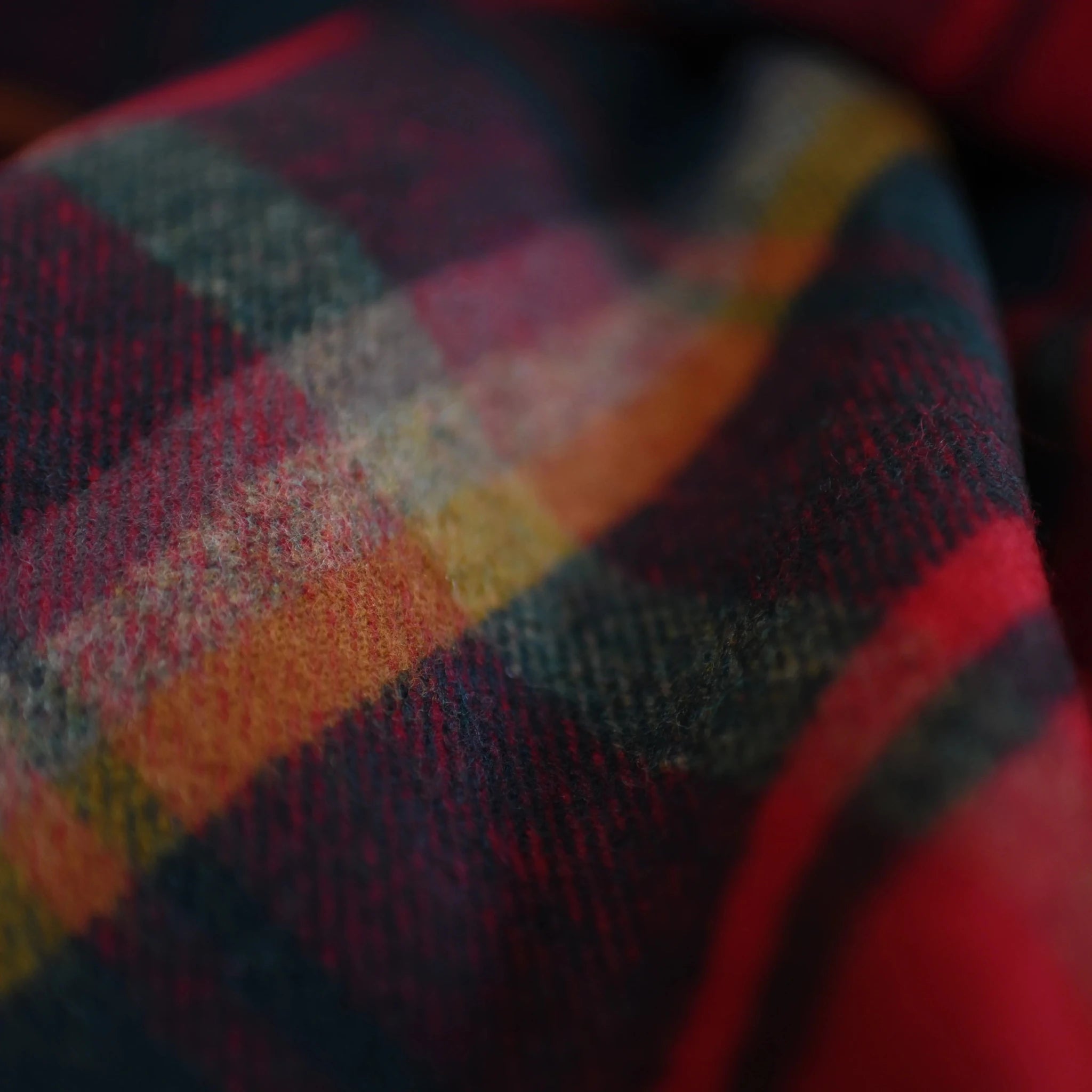 A close-up of the Auld Stock Lambswool Blanket by Campbell's of Beauly showcases its soft, woven texture and vibrant plaid pattern in red, yellow, green, and blue tones.