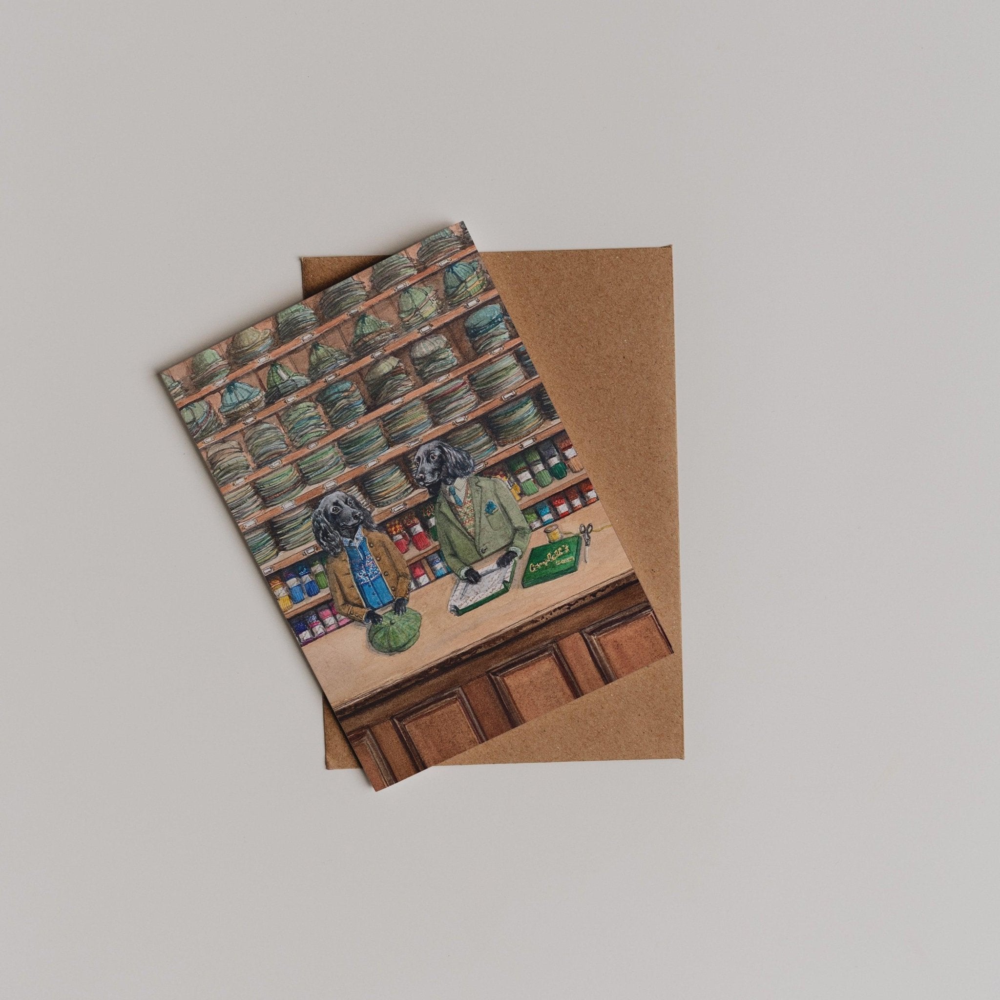 The Campbells Hats Greeting Card by Campbells of Beauly features two dogs in clothes behind a grocery counter—an adorable design that makes a charming thank you note. Includes a brown envelope and arrives against a plain background.