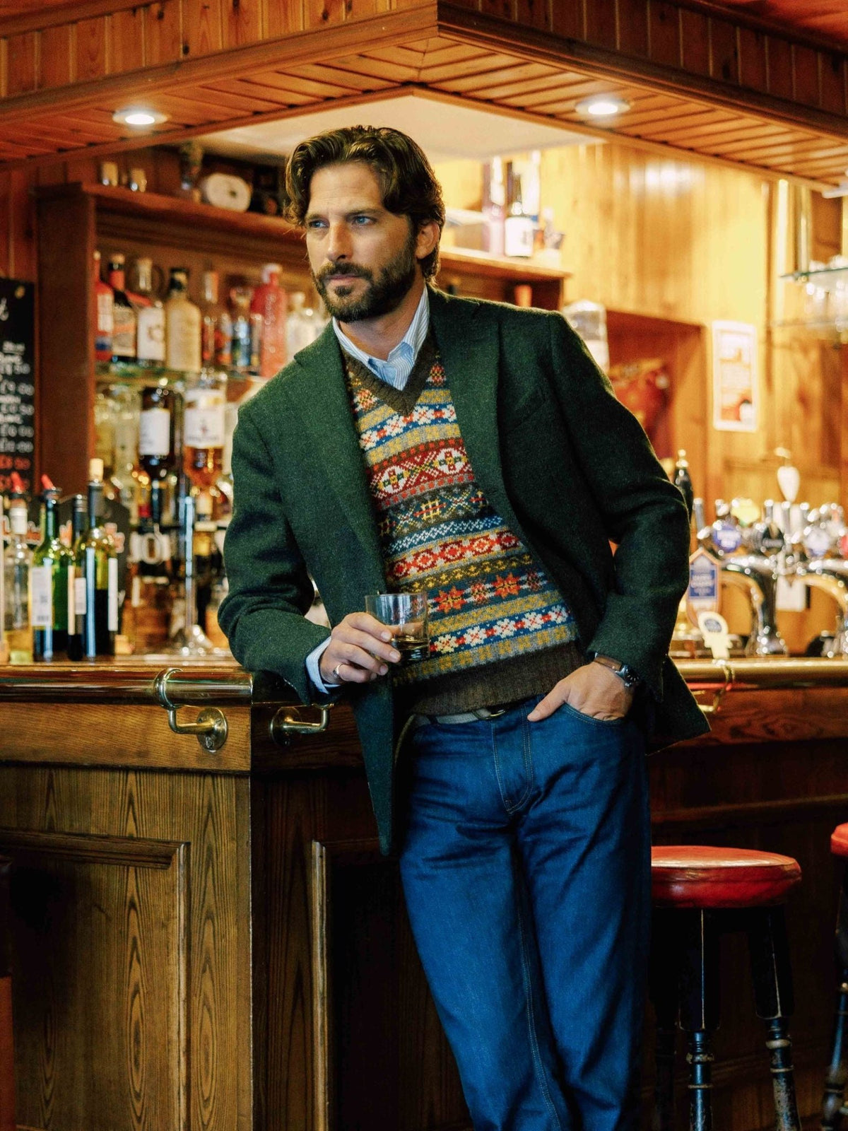 A man in a Campbell's of Beauly Harris Tweed Jacket stands at the bar, holding a glass of alcohol.