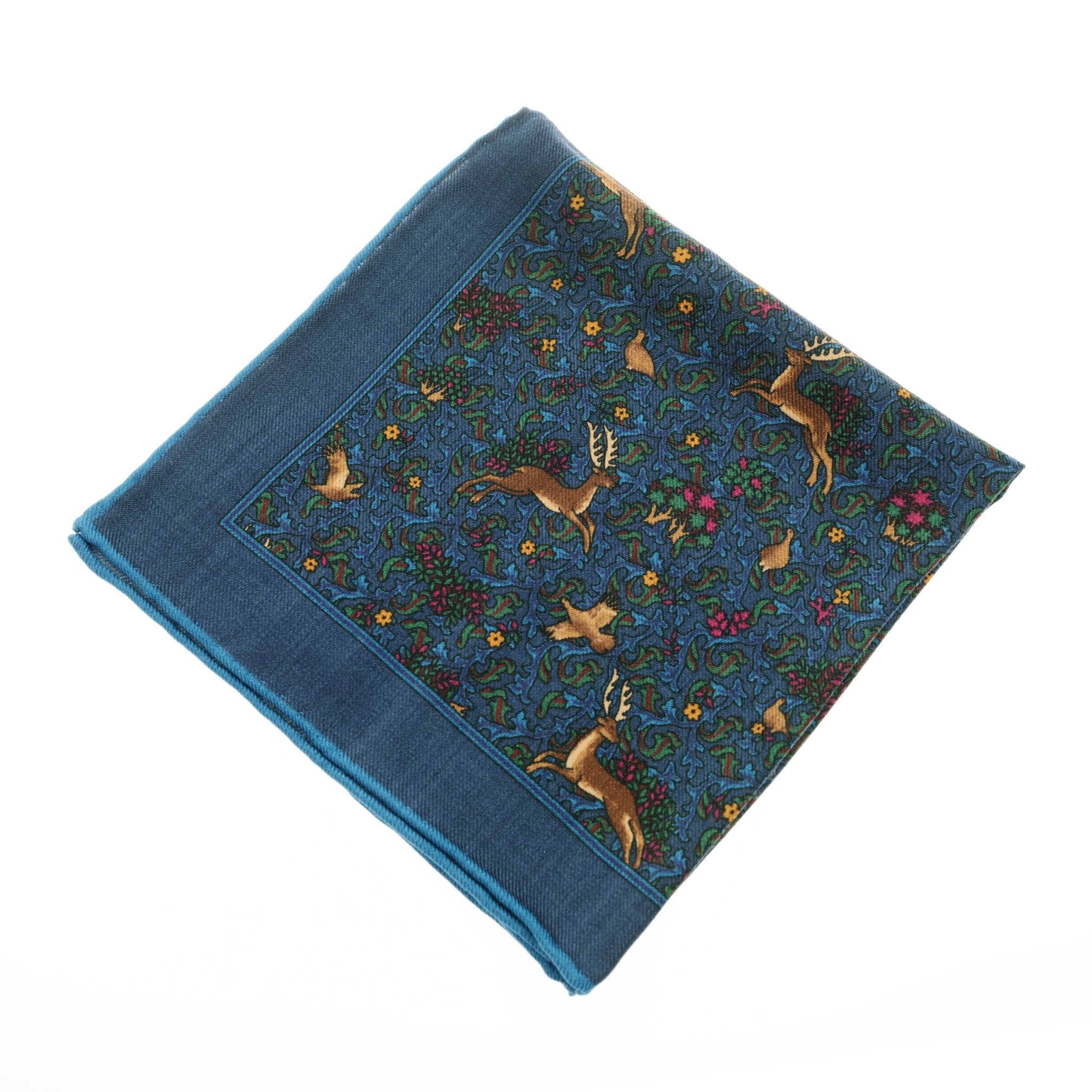 The Wool Hank by Campbells of Beauly is a blue wool handkerchief featuring deer, rabbits, and flowers with solid blue borders and hand-rolled edges—a timeless accessory against any white background.