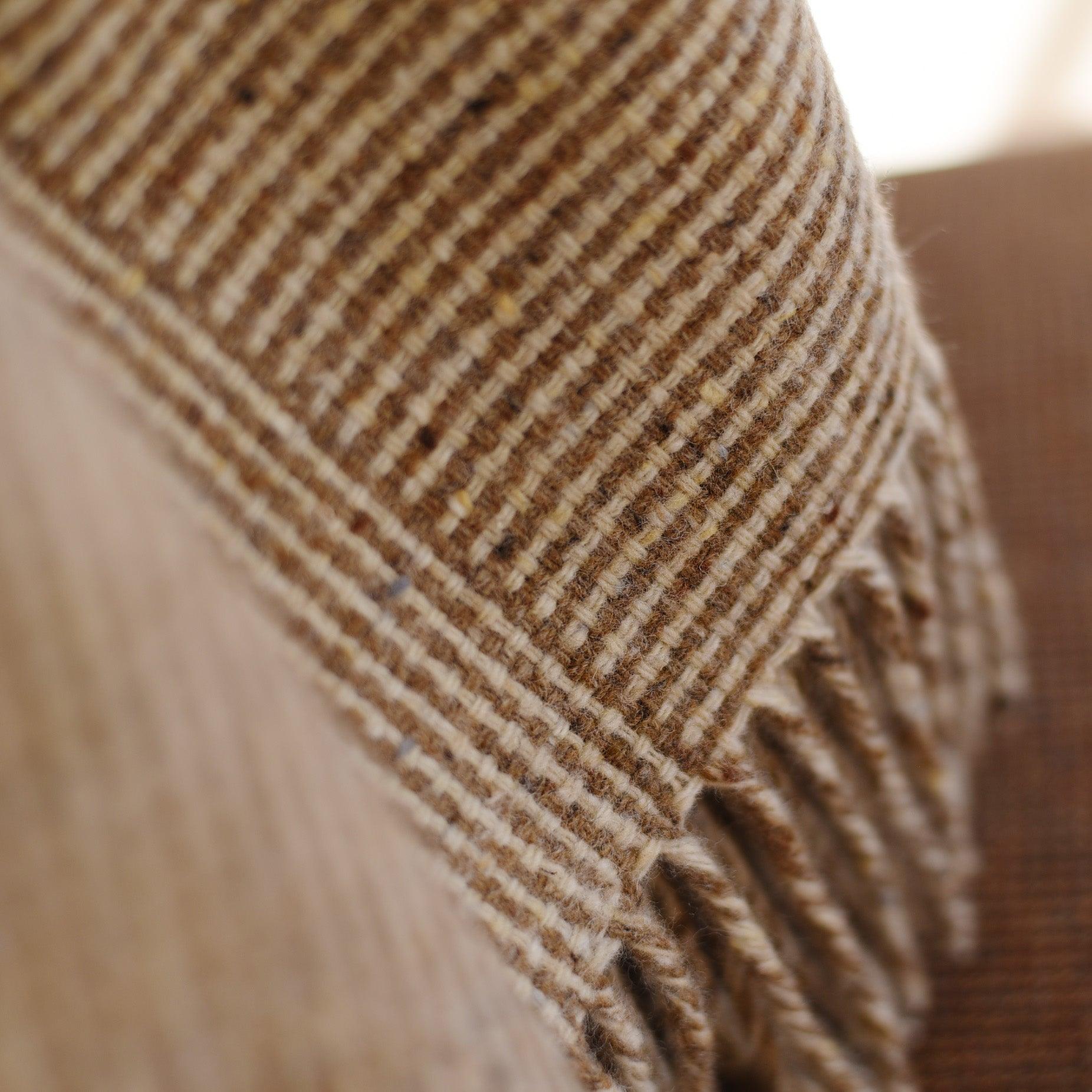 Close-up of the Cabrich Lambswool Throw by Campbells of Beauly, featuring brown and beige stripes, visible texture, and soft fibers. The detailed image showcases the throws classic basket weave pattern with fringe on one edge.