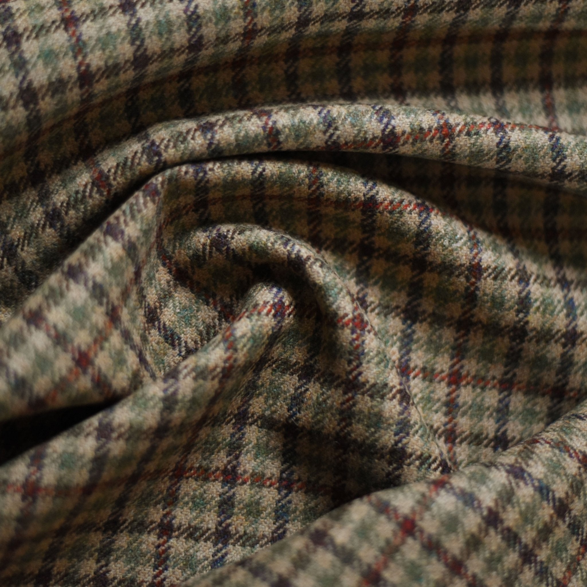 A close-up of Campbells of Beauly House Tweed 84934 shows crumpled Saxony Tweed fabric with a green, brown, red, and cream check pattern—its rich texture reflects the bespoke tailoring heritage of the Scottish Borders.