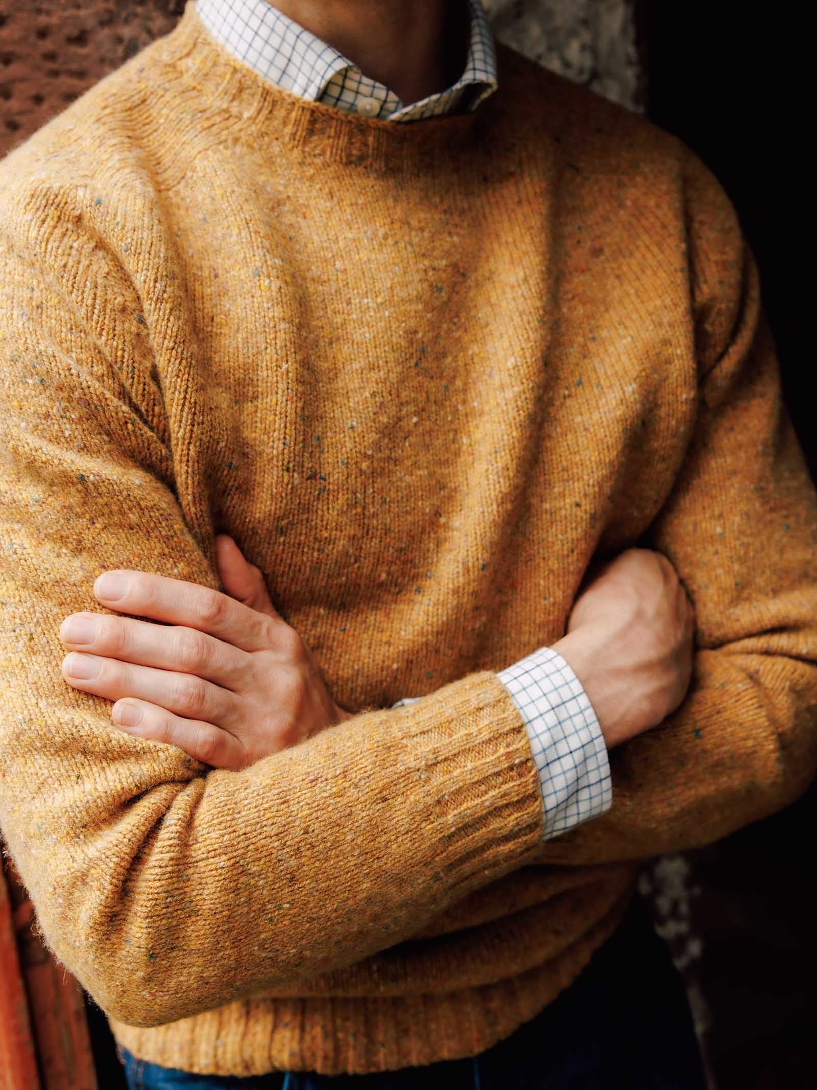 A person wearing a mustard yellow Campbell’s of Beauly Donegal Lambswool Crew Neck Jumper, crafted from luxurious lambswool and made in Scotland, stands with arms crossed over a white checkered shirt.