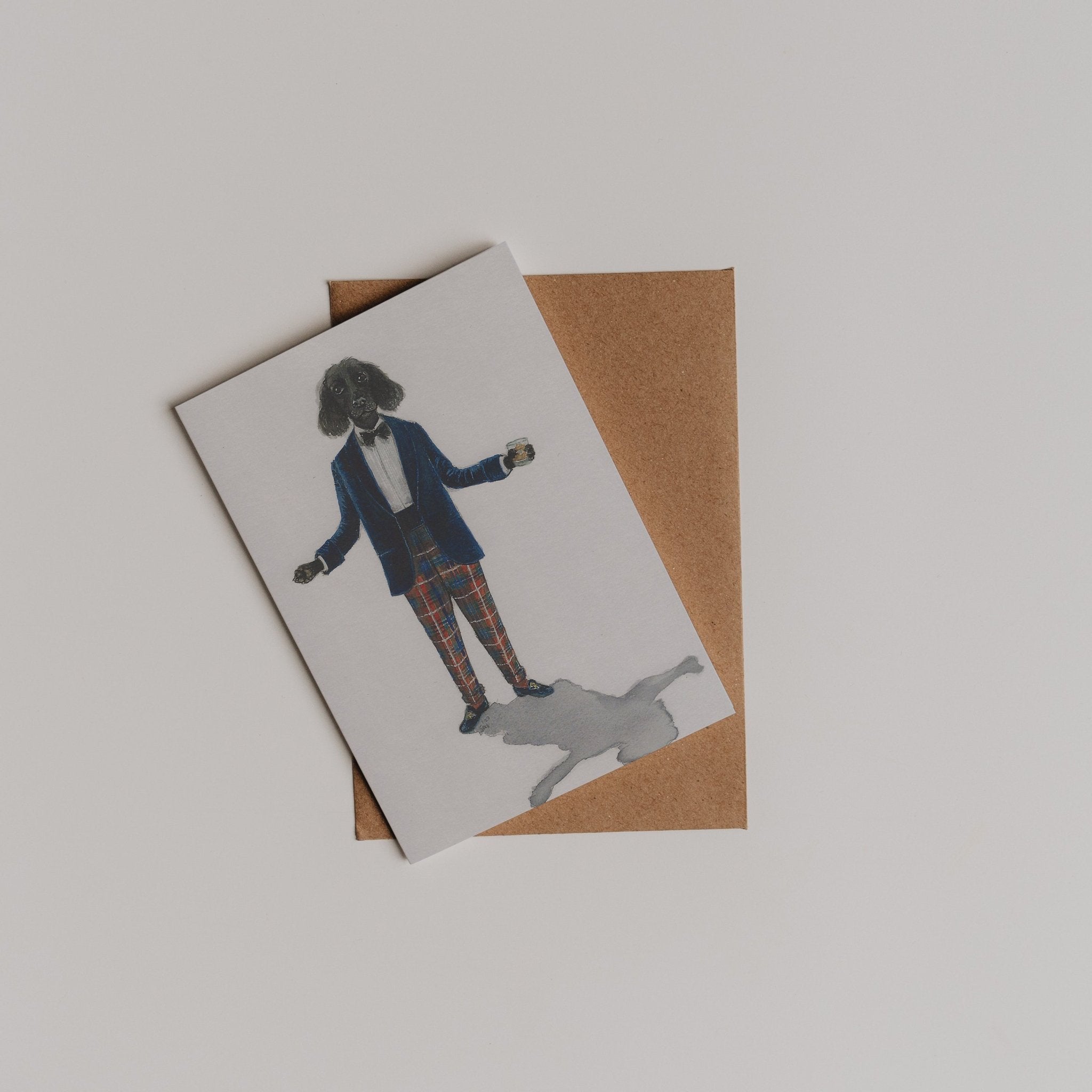 The Campbell’s of Beauly Evening Wear Greeting Card shows a dog in a blue blazer and plaid pants, standing upright atop a brown envelope—ideal for a charming thank you note or celebrating classic style.