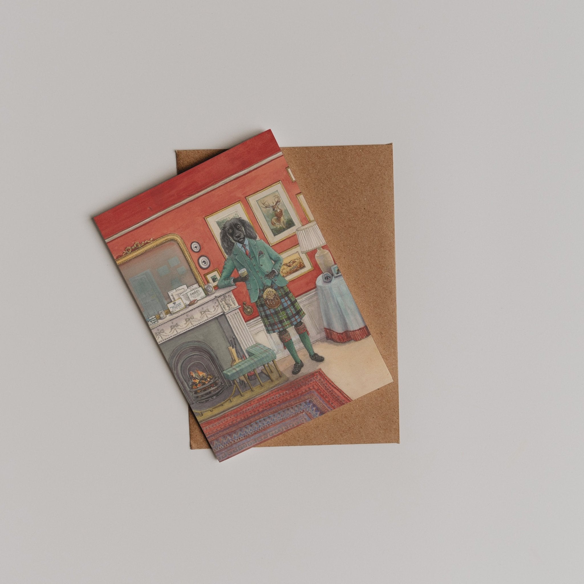 The Fireside Dram Greeting Card by Campbell's of Beauly features a dog in clothes standing in a red-walled room, resting on a brown envelope—a charming thank-you card designed by Sophie Murray.