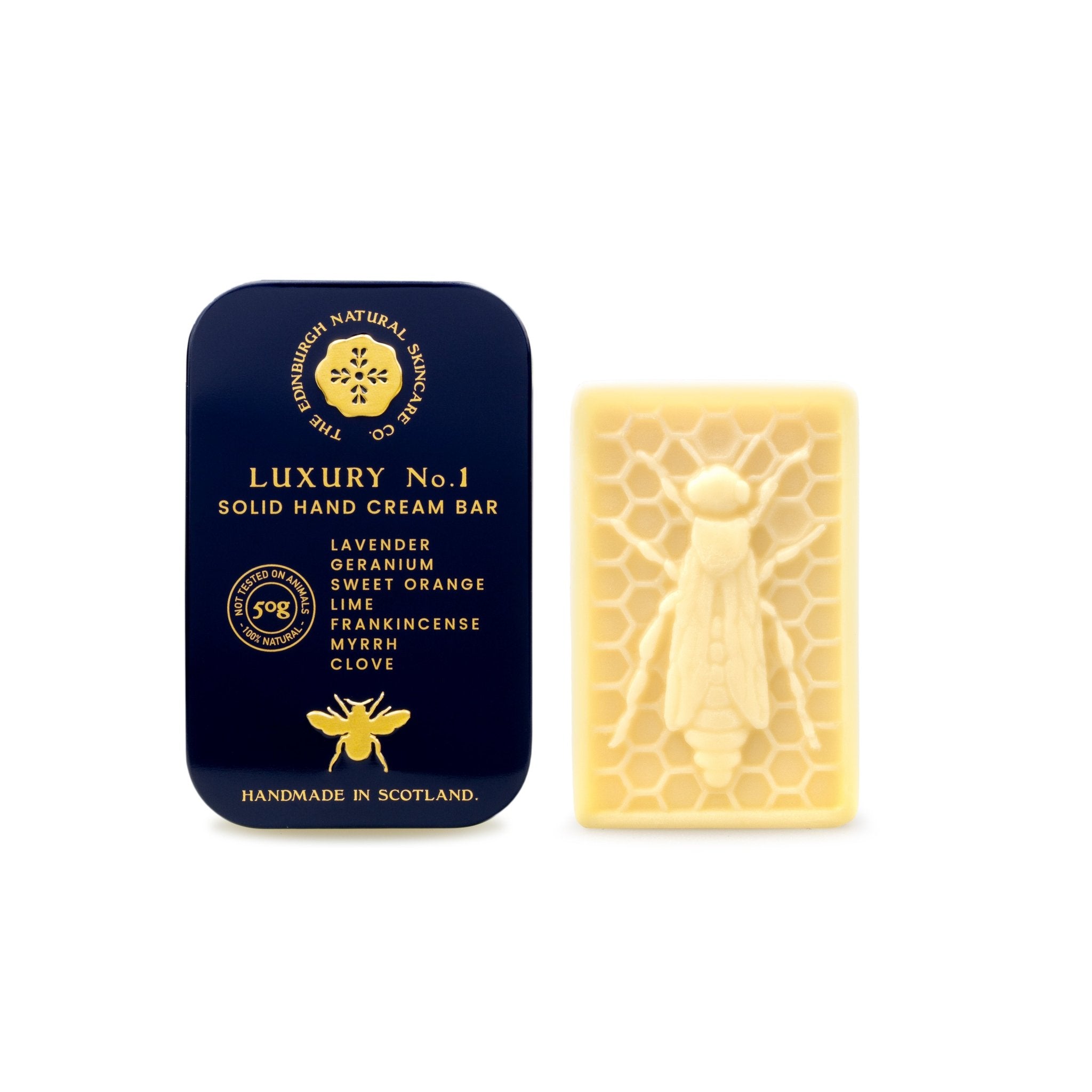 A dark blue tin labeled "Luxury No. 1 Solid Hand Cream Bar" by The Edinburgh Natural Skincare Company sits beside a cream bar embossed with a honeycomb and bee, offering handmade natural hand moisturiser from Scotland.