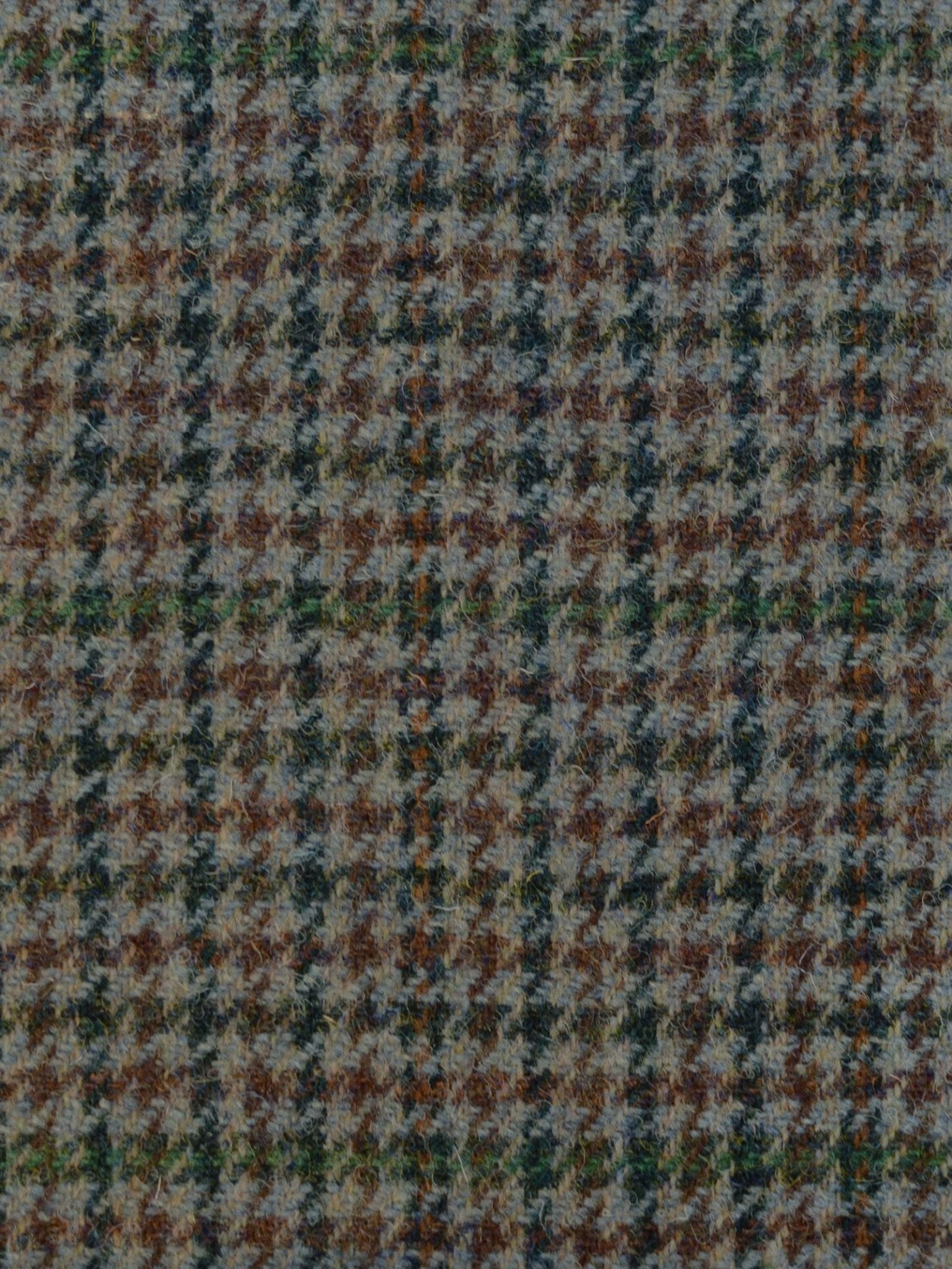 Close-up of Harris Tweed 93900 by Campbell's of Beauly, featuring a classic houndstooth pattern in browns, greens, grays, and beige—highlighting textured wool fibers and traditional Scottish craftsmanship.