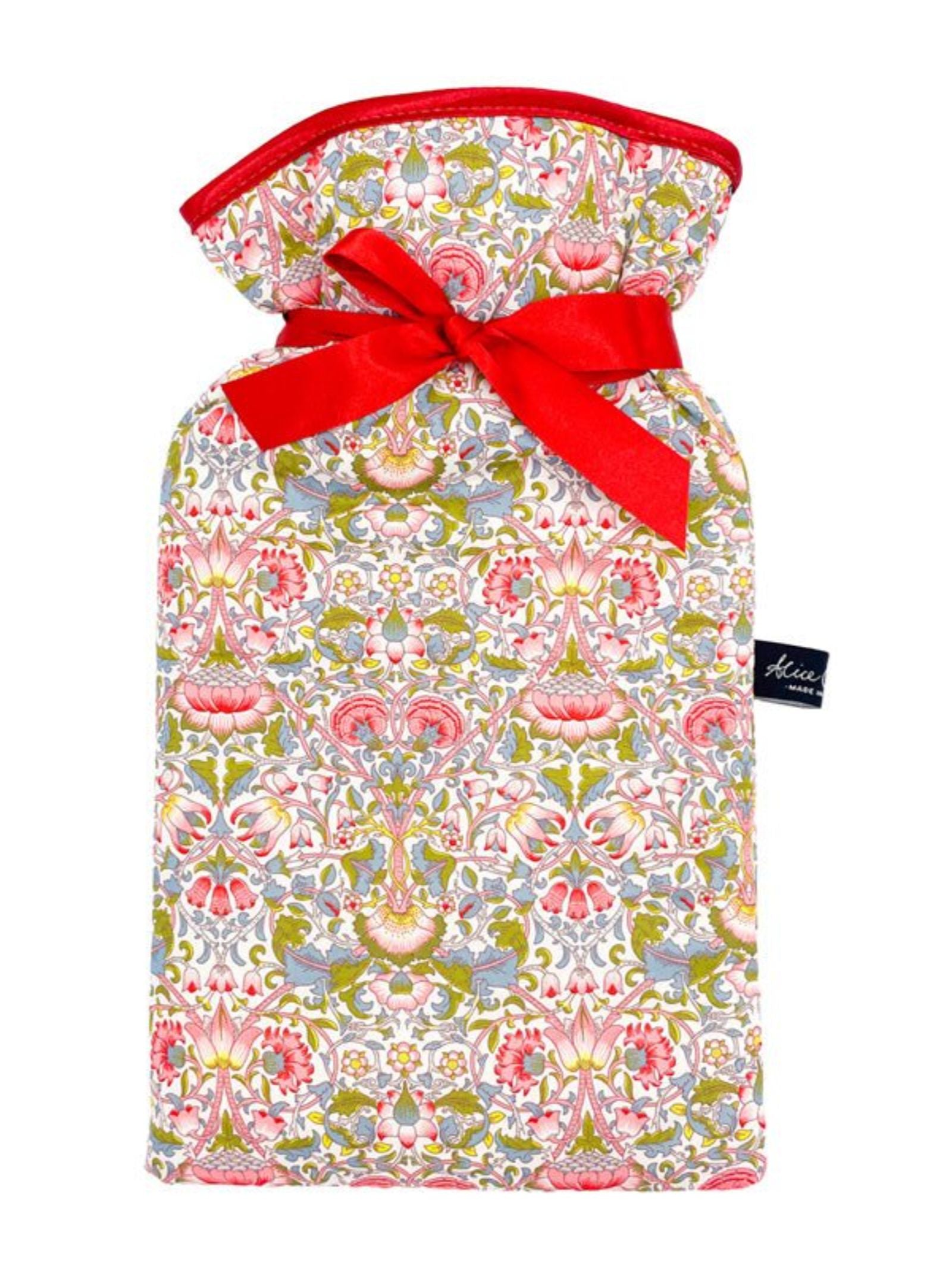 The Alice Caroline Liberty Print Hot Water Bottle features colorful red, pink, green, and yellow floral Liberty cotton fabric, tied at the neck with a bright red ribbon and finished with a small black side label.