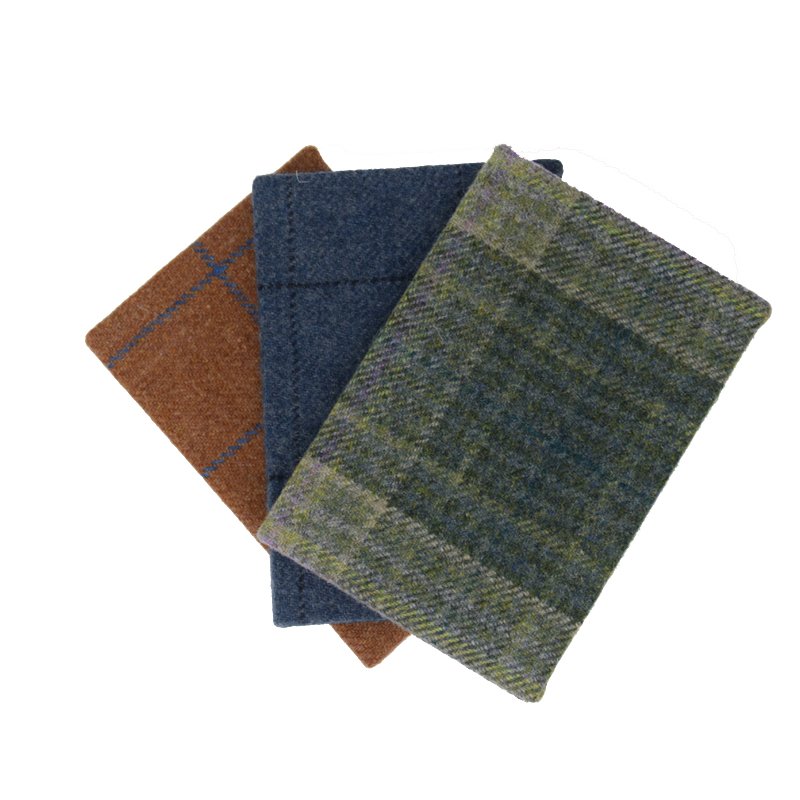 Three Campbell's of Beauly Tweed Notebooks in brown, blue, and green plaid/solid wool covers overlap on a white surface. Each A5 eco-friendly notebook features plain pages for versatile use.