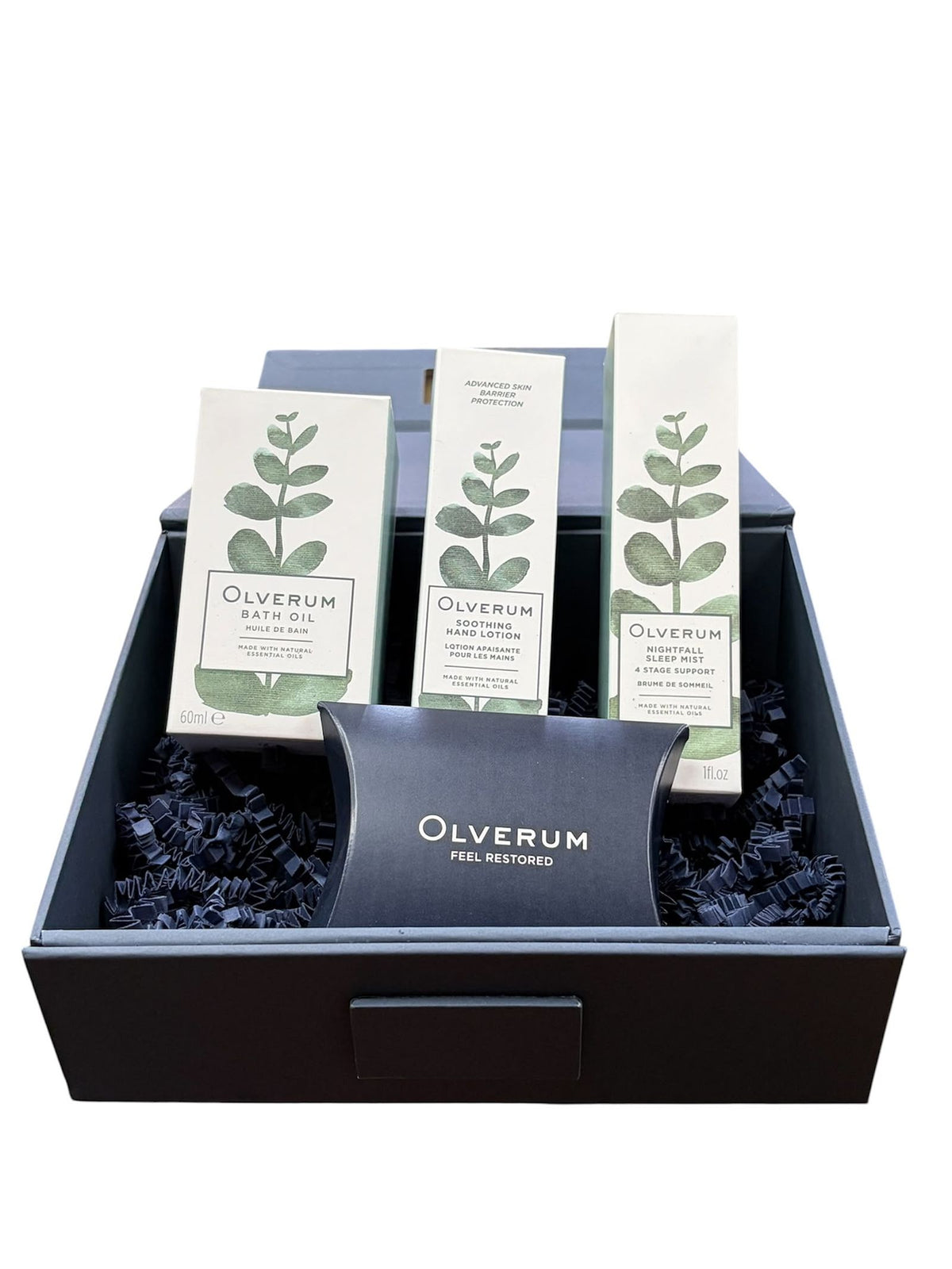 Three Olverum Restore and Revive skincare product boxes and a small pillow box nestled inside an open gift box filled with dark paper crinkle filler.