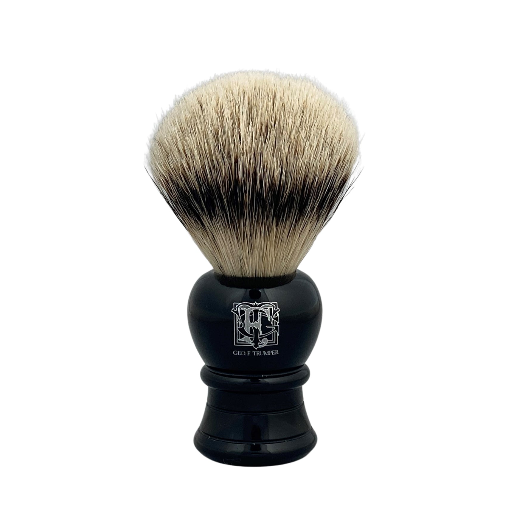 The Geo. F. Trumper Black Shaving Brush features dense, light-colored bristles and a sleek black handle, standing upright against a white background—designed for a rich, luxurious lather and comfortable shave.