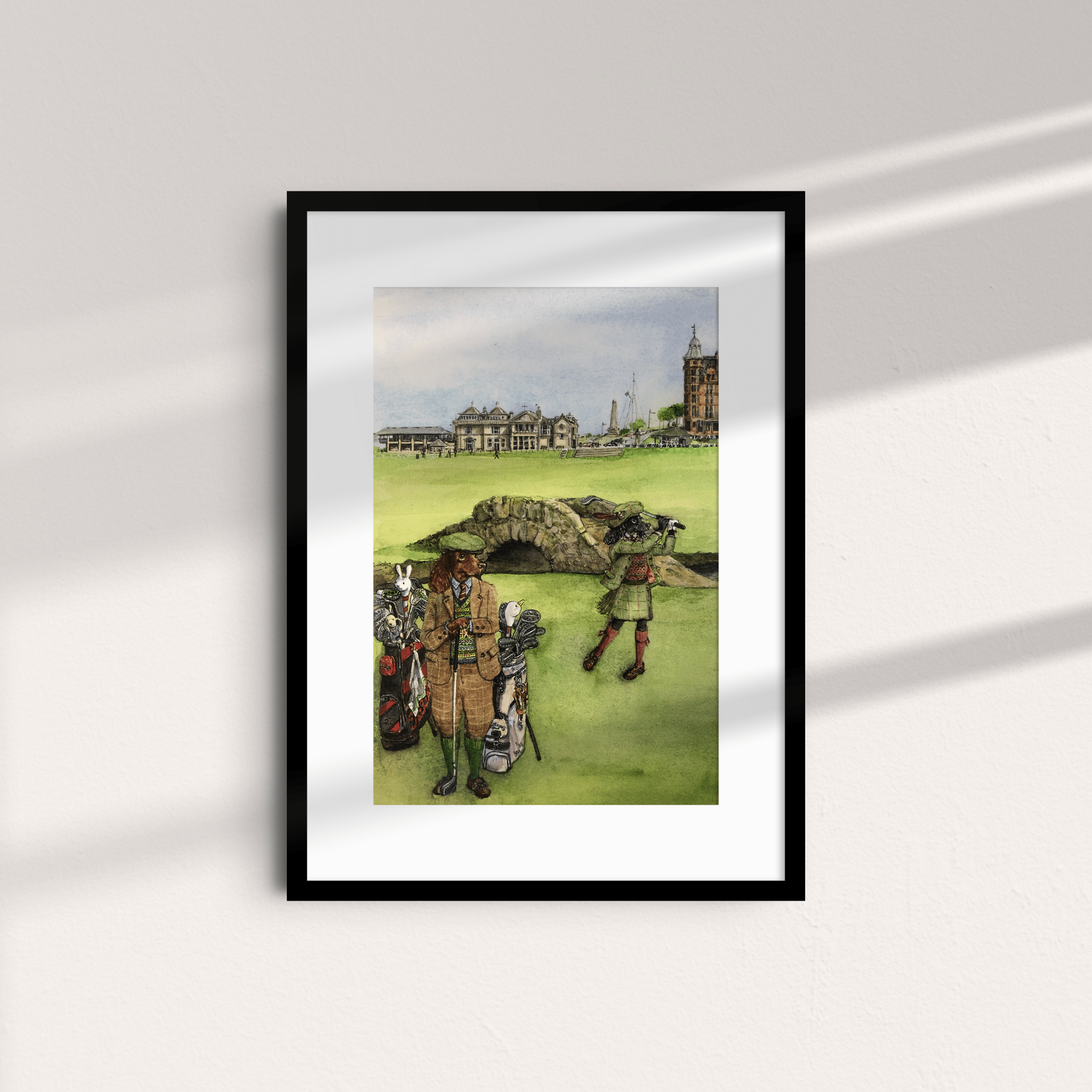 The Swilcan Bridge Cocker Unframed Print by Campbells of Beauly features two golfers in period attire on a lush course, with the iconic stone bridge and historic buildings behind, sunlight casting diagonal shadows on a light wall.