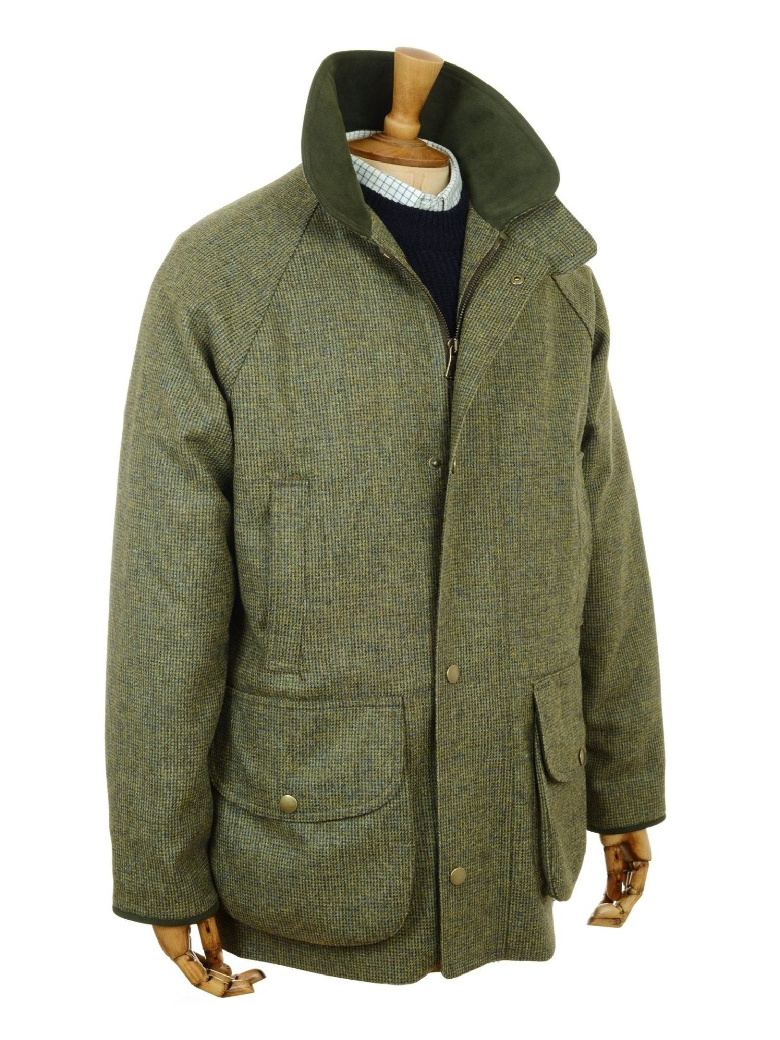 A Campbell’s of Beauly Tweed Field Coat in green tweed features a high collar, buttoned front, and two large pockets. Shown on a mannequin layered over a white sweater, this classic outdoor jacket is made in the UK.