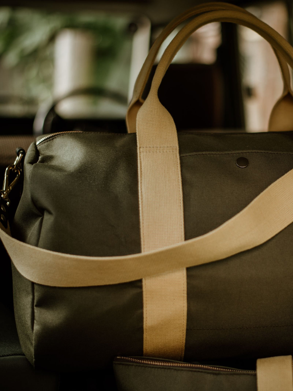 The Campbell's of Beauly Utility Medium Duffle, made from heavy-duty canvas with beige straps, rests inside a vehicle. Its dark green color stands out against the blurred background visible through the window.