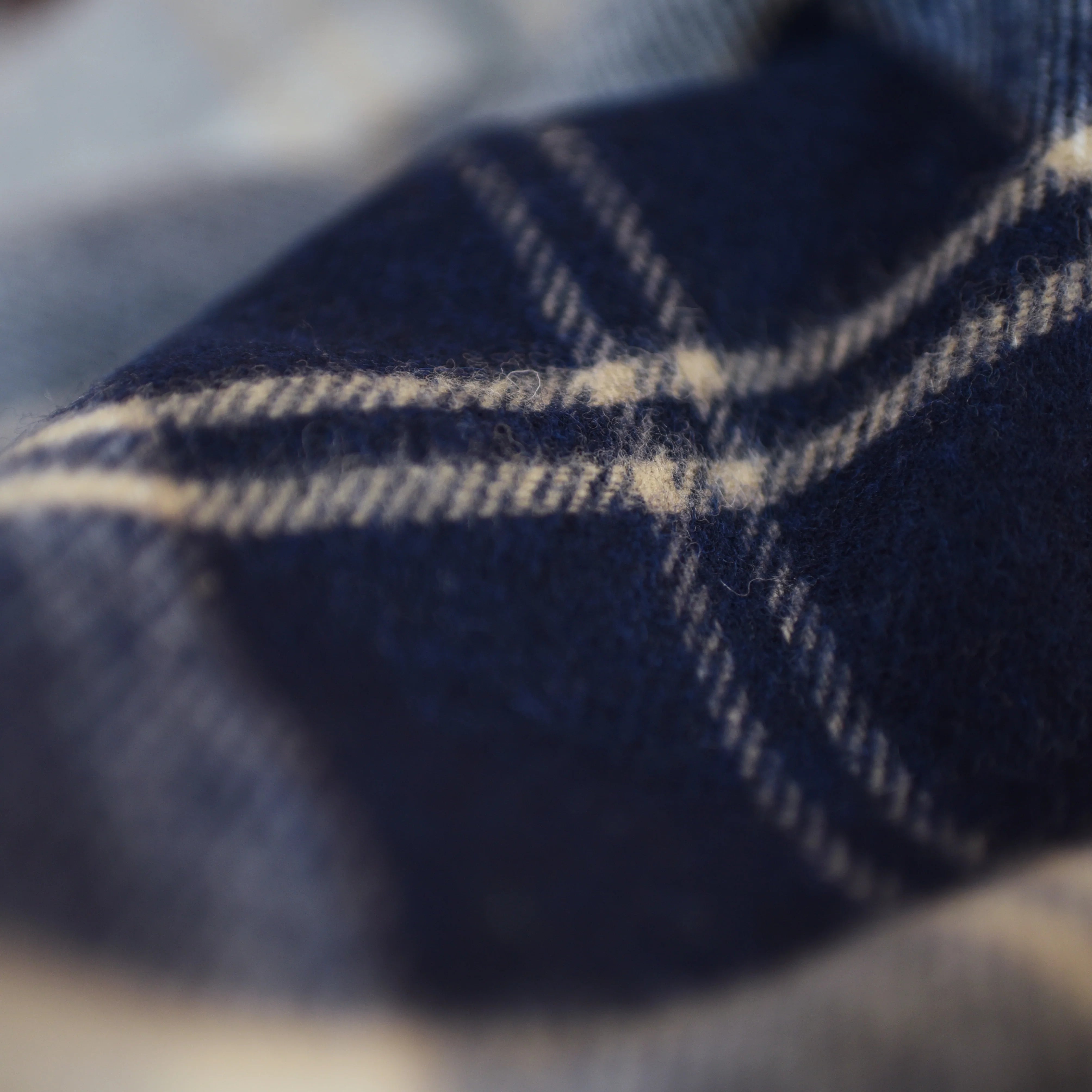 A close-up of the Lambswool Tartan Blanket by Campbell's of Beauly shows soft, fuzzy fabric in a navy and cream plaid, emphasizing the intersecting lines and quality craftsmanship.