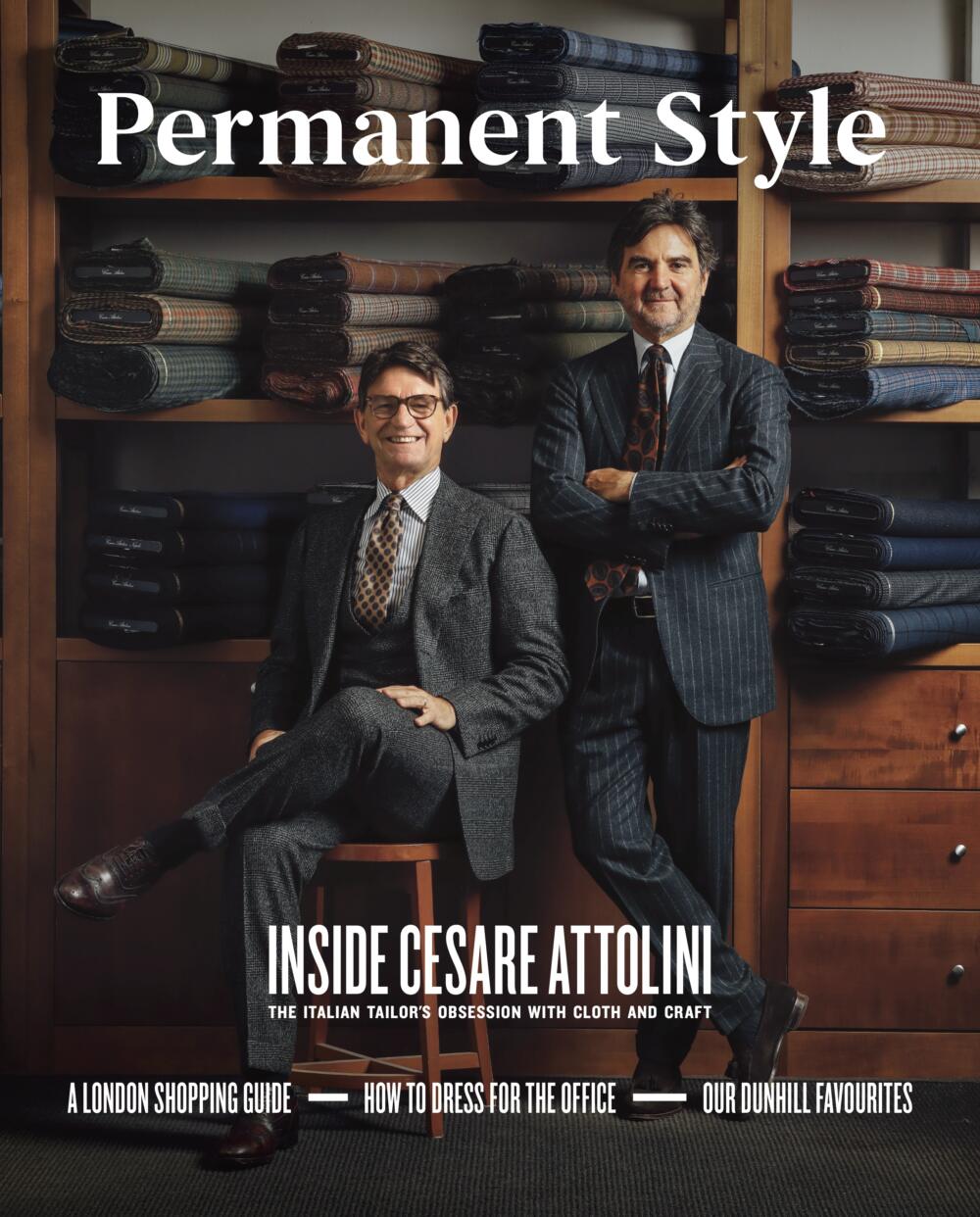 Two men in tailored suits stand before shelves of fabric rolls. On the cover of Permanent Style Magazine, Issue 2 by Permanent Style: Inside Cesare Attolini—revealing one of the world’s finest tailoring houses.