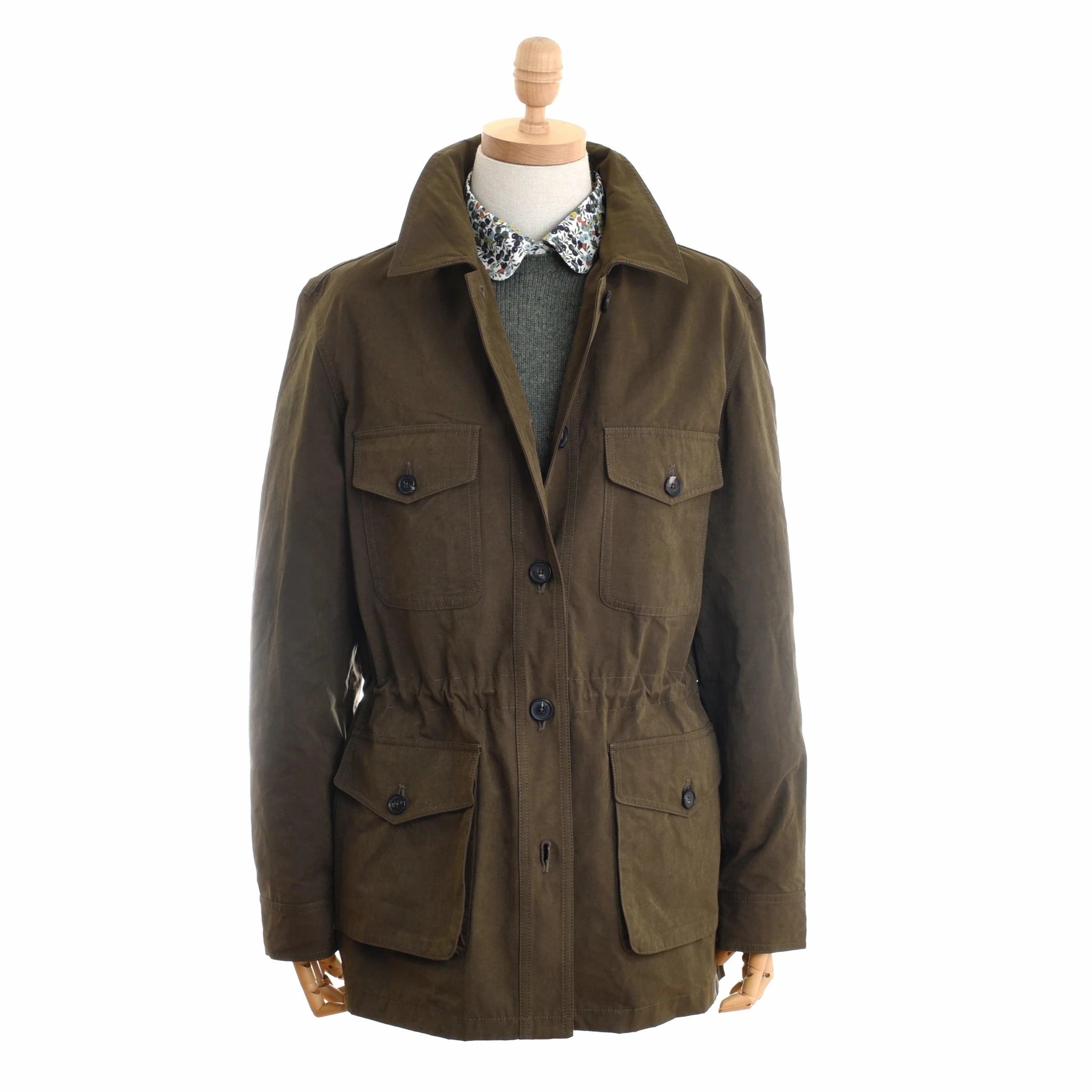 A mannequin wears a Campbell's of Beauly Auld Stock Aigas Field Jacket in olive green water-repellent peach skin, layered over a green sweater and floral collared shirt, set against a plain white backdrop.