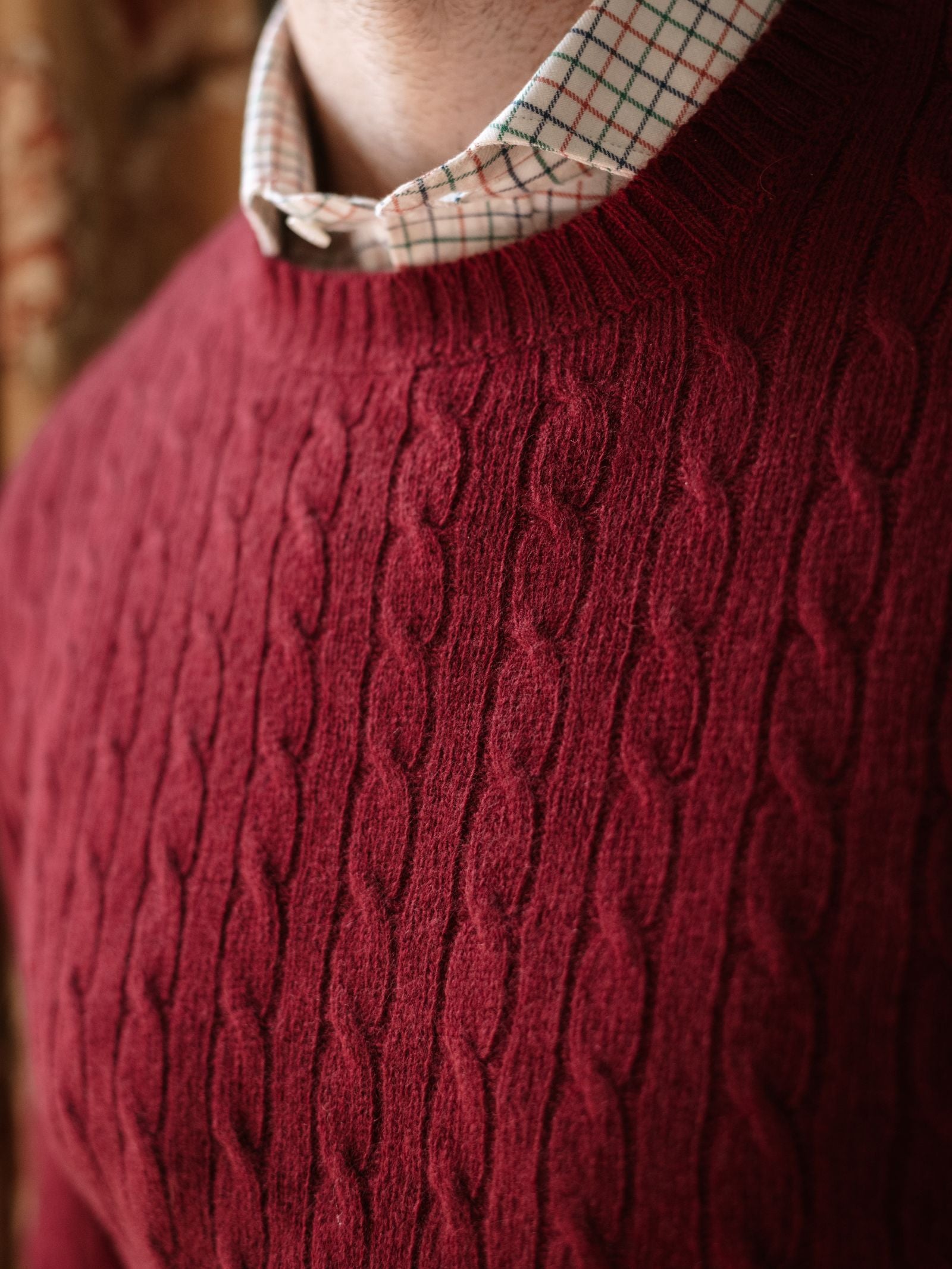 Close-up of a person wearing Campbell's of Beauly's Cashmere Cable Crew Jumper in red over a white, small plaid-collared shirt. Only the lower face and neck are visible.