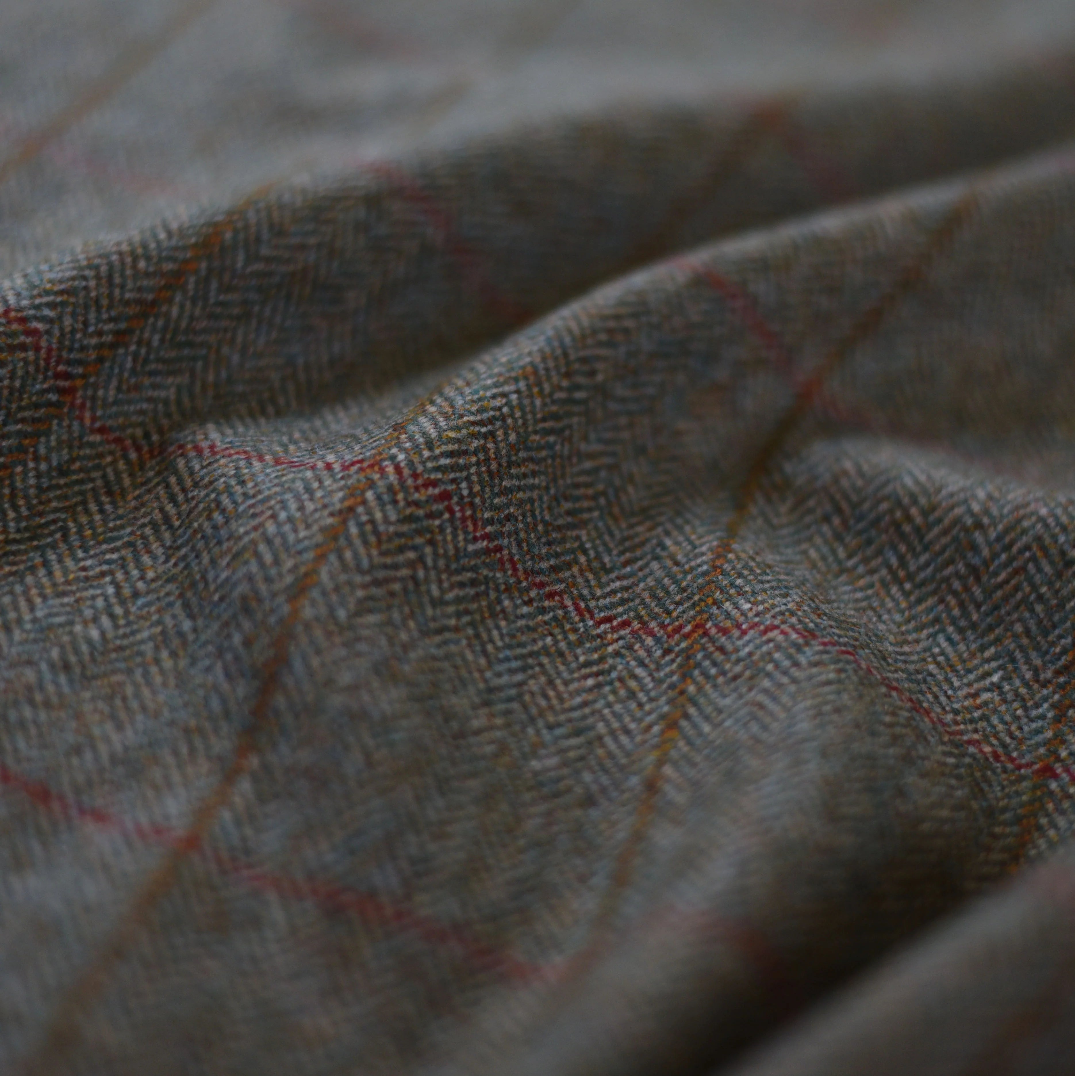 Close-up of House Tweed 62527 by Campbell's of Beauly, showing traditional tweed with a subtle herringbone pattern and thin red grid lines over a muted gray-brown background. The fabric appears slightly folded.