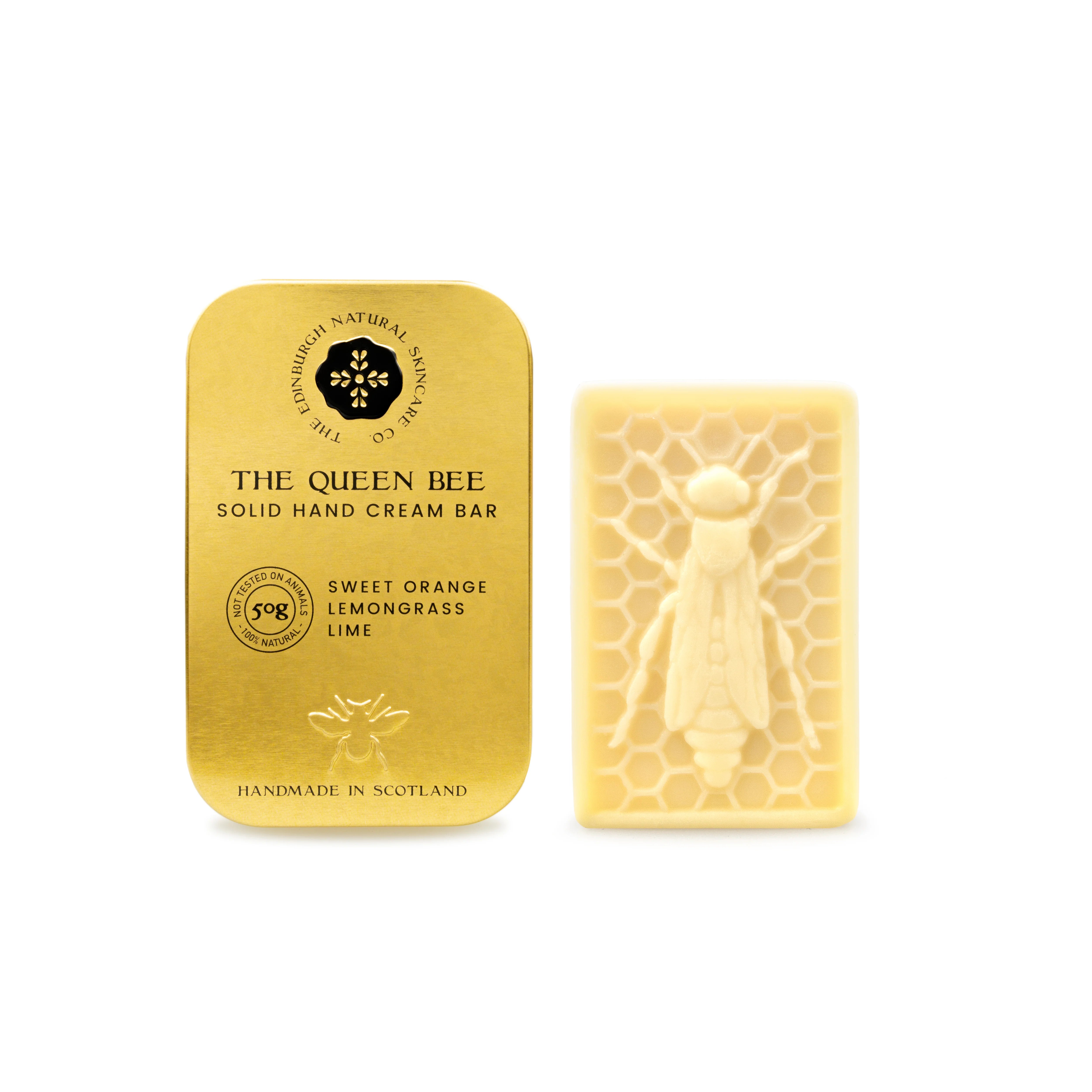 A gold tin of The Edinburgh Natural Skincare Company’s Queen Bee Hand Cream Bar sits next to a yellow, bee-shaped hand cream bar with a honeycomb pattern.