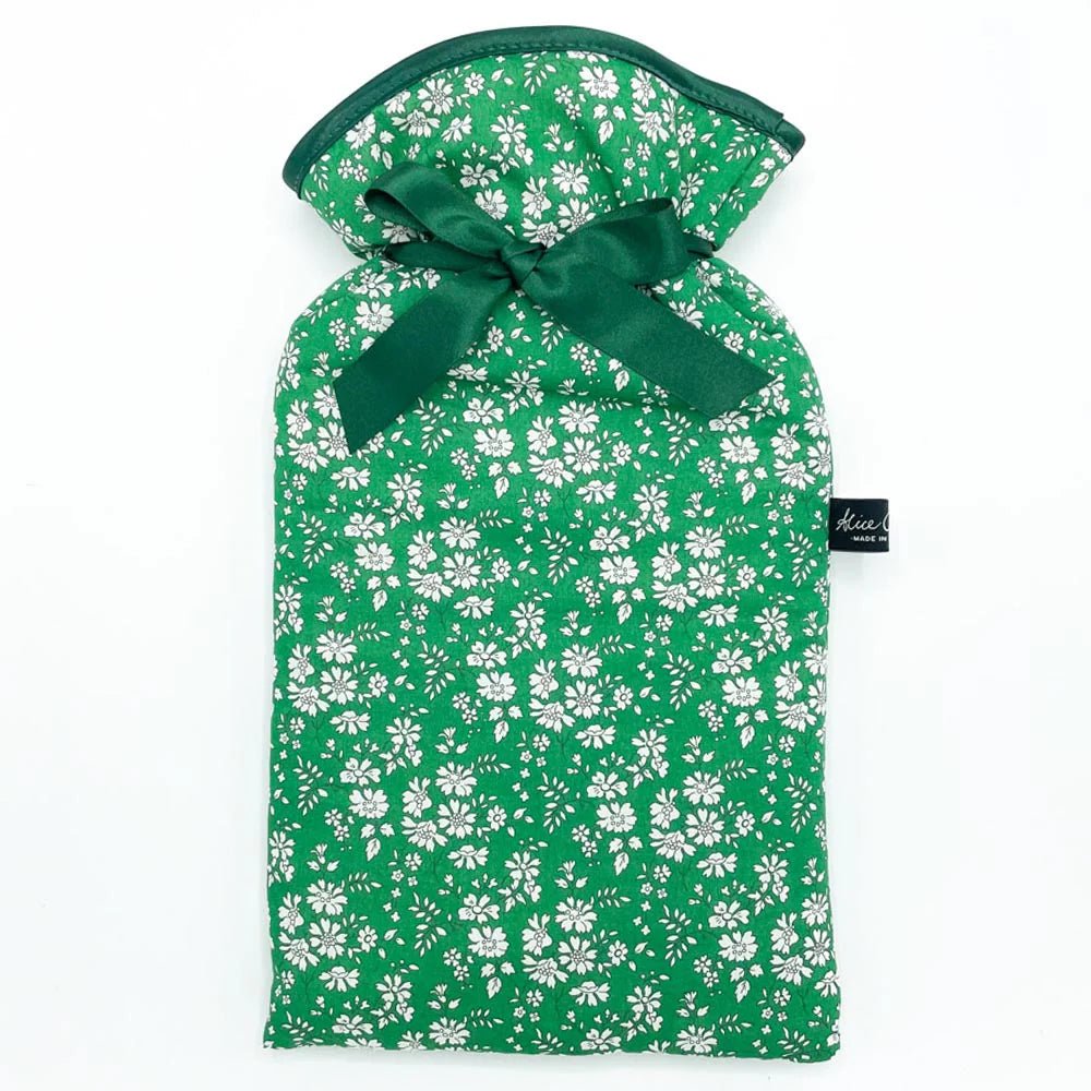 The Auld Stock Liberty Print Hot Water Bottle by Alice Caroline features a green, white floral Liberty cotton cover, finished with a dark green ribbon bow and a small black side tag.