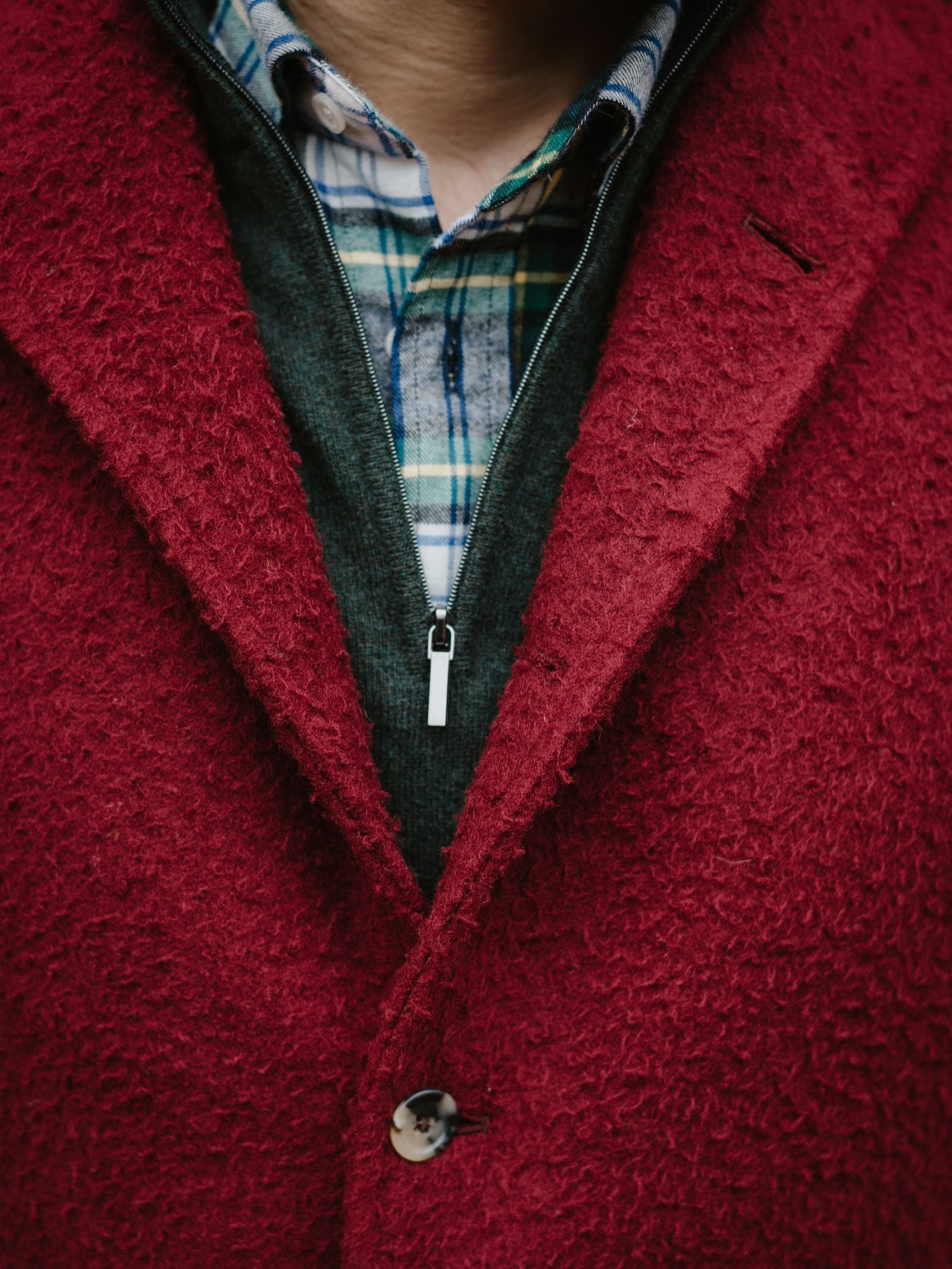A close-up of a person wearing the Campbell's of Beauly Casentino Fleece Gilet over a dark zip-up sweater and blue-green plaid shirt. The layered fabrics are in focus, with no face shown.