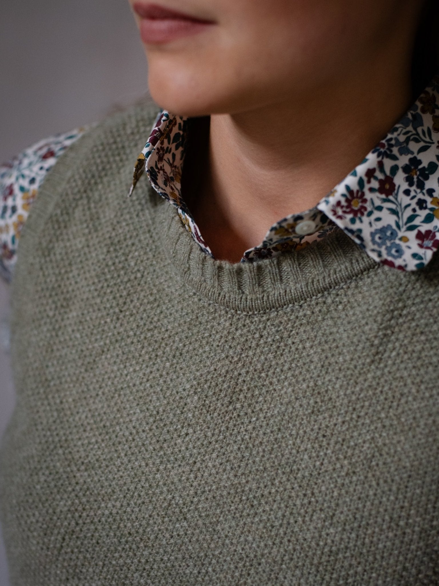 A person wears the Campbell's of Beauly Moss Stitch Crew Tank in green over a floral-collared shirt, shown from the shoulders up with their face partially visible and lips closed.