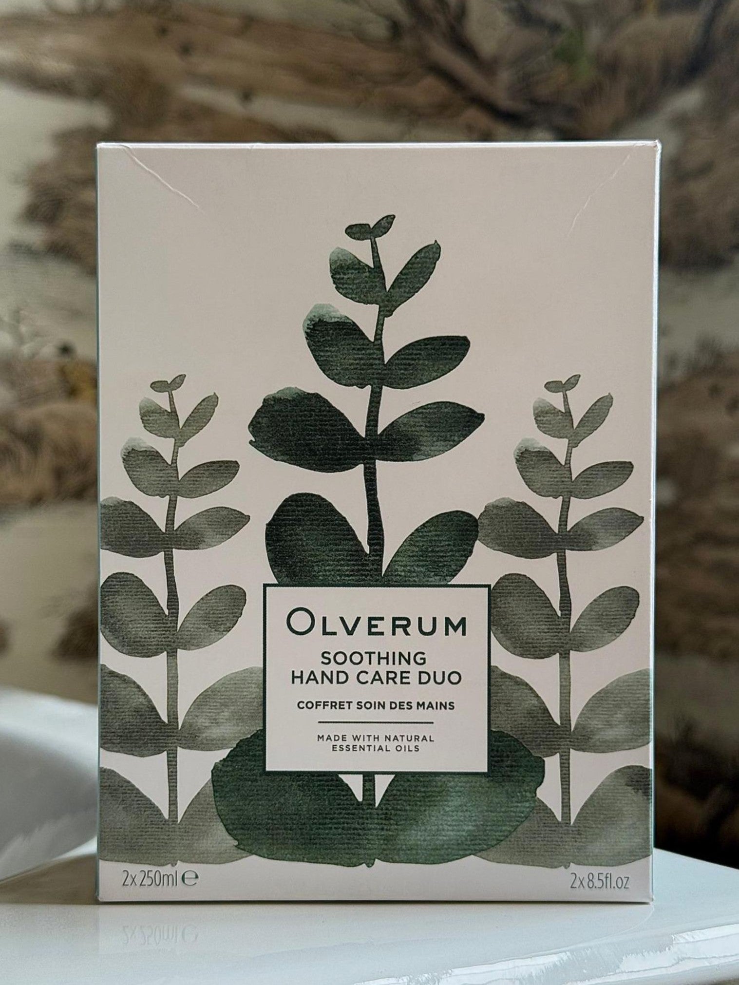 A box of OLVERUM Hand Care Duo, adorned with green eucalyptus illustrations, contains two 250 ml bottles made with natural essential oils.