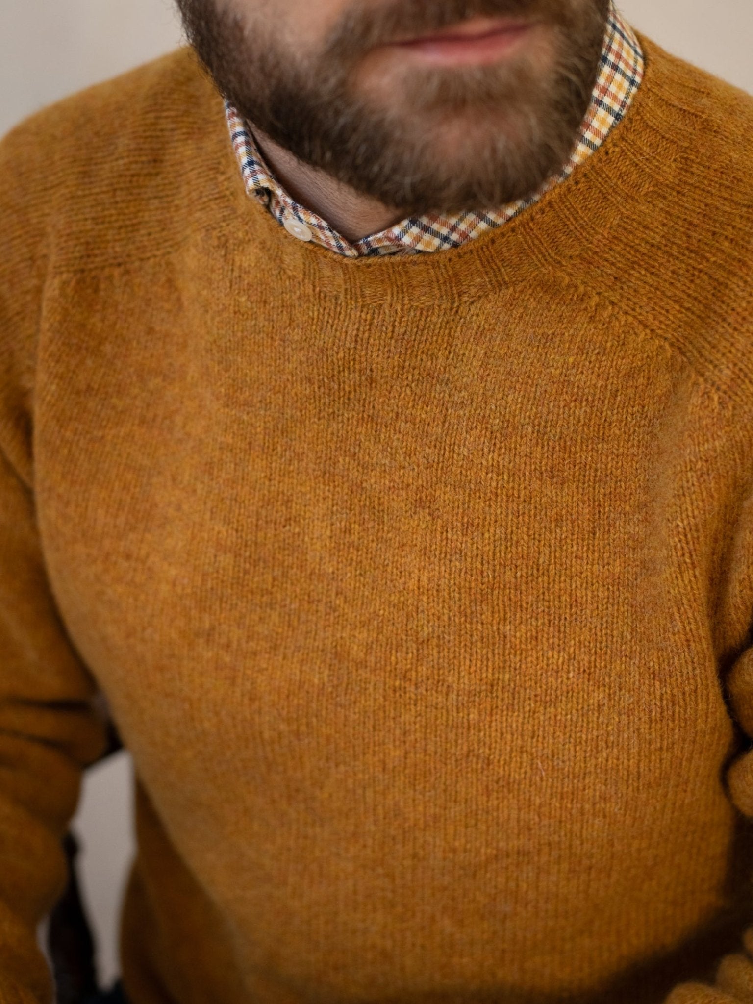 A man with a short beard wears the Campbell's of Beauly Shetland Jumper in mustard brown over a plaid collared shirt. The photo is cropped to show only his lower face, neck, and upper torso.