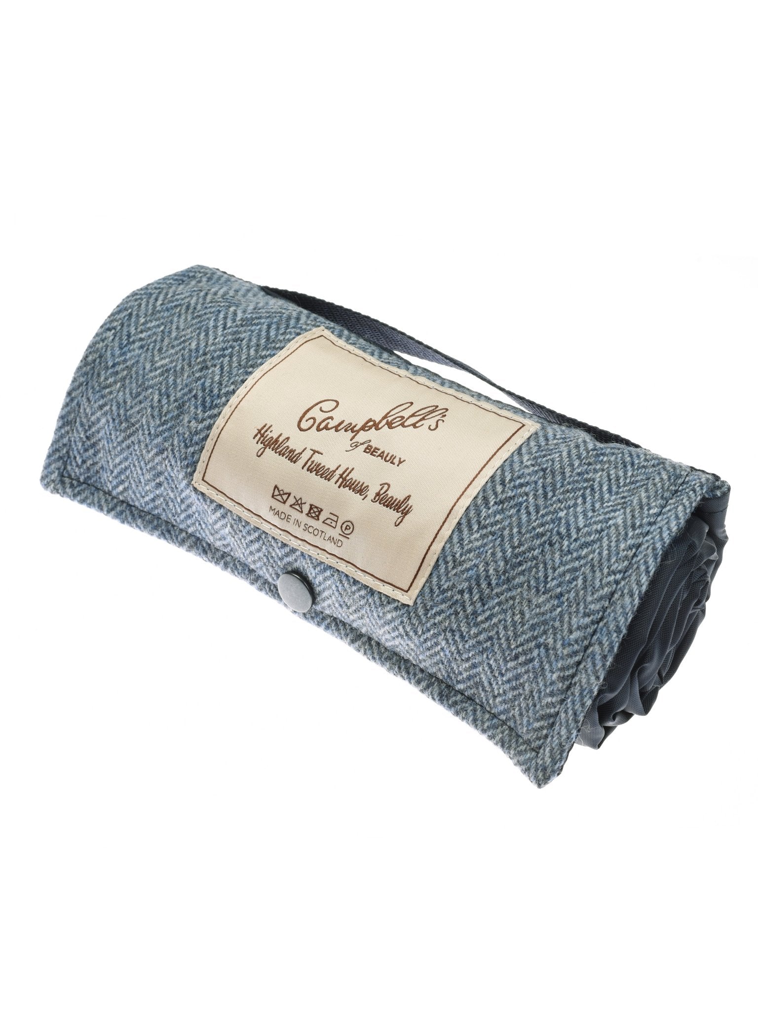 The Walker Camper Picnic Rug by Campbell's of Beauly is a blue-gray herringbone British wool blanket with a tan label and care symbols, secured by button and strap for easy carrying.