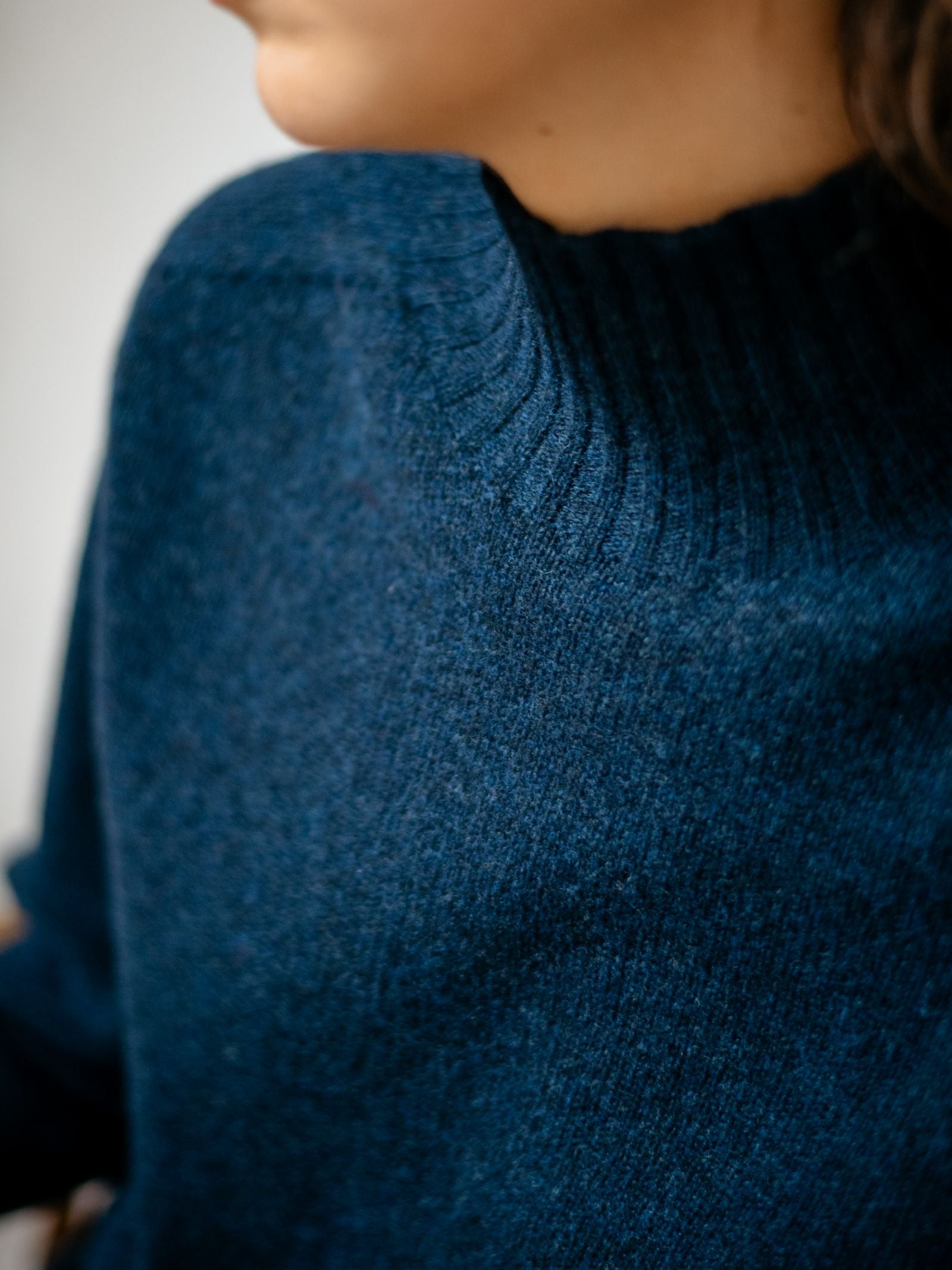 A close-up shows the lower face and neck of a person wearing the Campbells of Beauly Geelong Lambswool Funnel Neck, a dark blue, ribbed knit sweater crafted in Scotland.