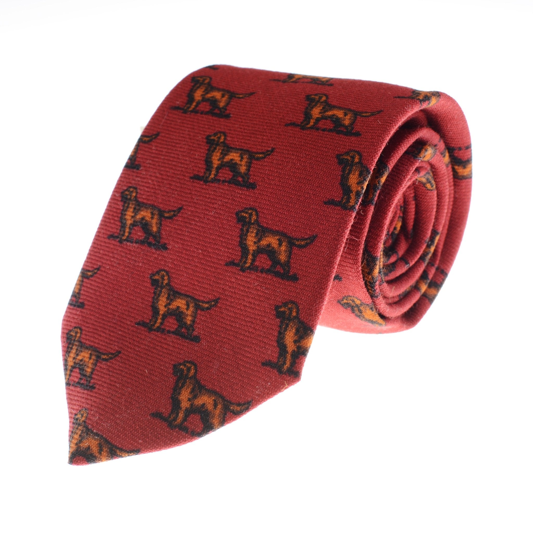 The Setter Dog Silk Tie by Campbell's of Beauly is a handmade UK silk tie in rich red, featuring a repeating brown dog countryside motif and shown rolled up on a white background.