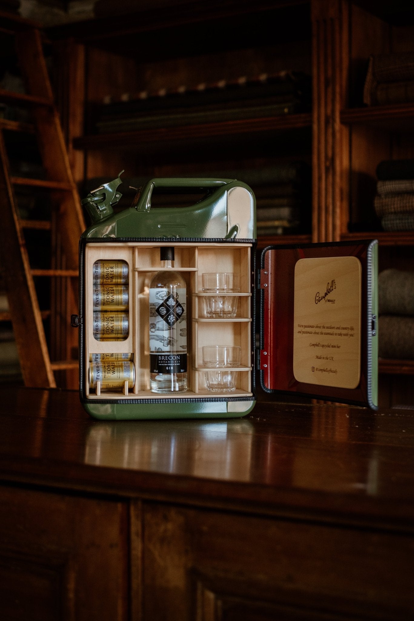 The Original Upcycled Mini Bar by Campbell's of Beauly is a handmade UK piece crafted from a repurposed jerry can, with its door open to show a bottle of gin, three tonic cans, and two glasses neatly arranged on the shelves.