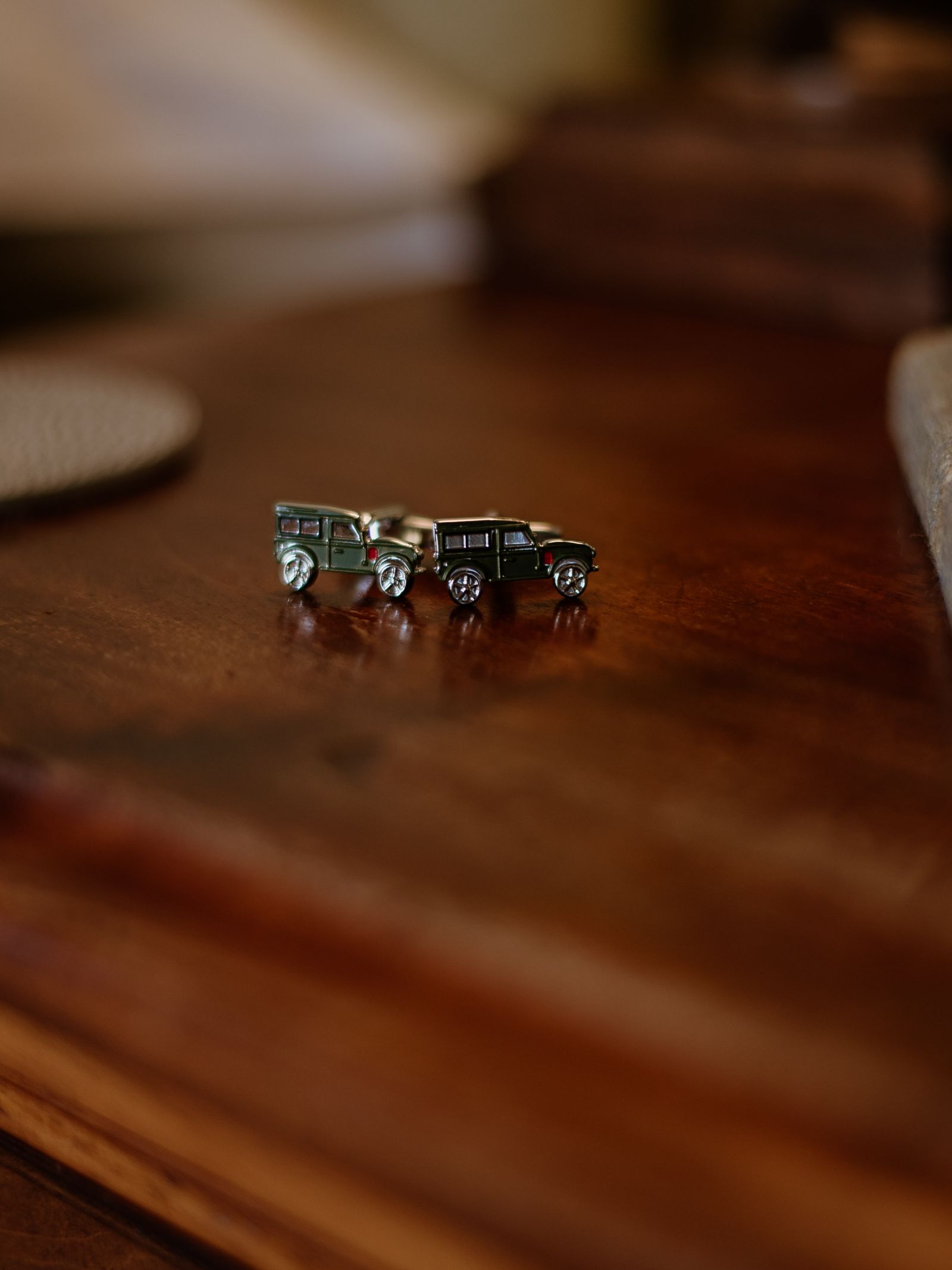 Campbell's of Beauly Land Rover Defender Cufflinks—two small, green vintage designs on a polished wooden surface—are the perfect Defender gift for car enthusiasts.