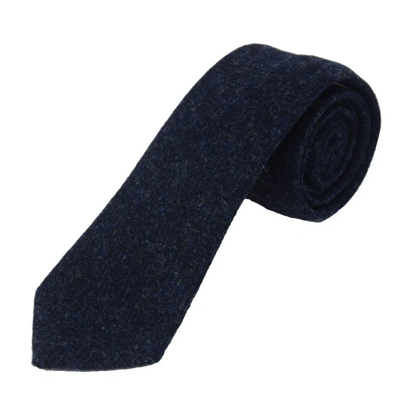 The Campbell's of Beauly Tweed Tie, handmade in the UK from dark navy blue wool, is rolled up on a white background to display its textured tweed fabric and pointed tip.