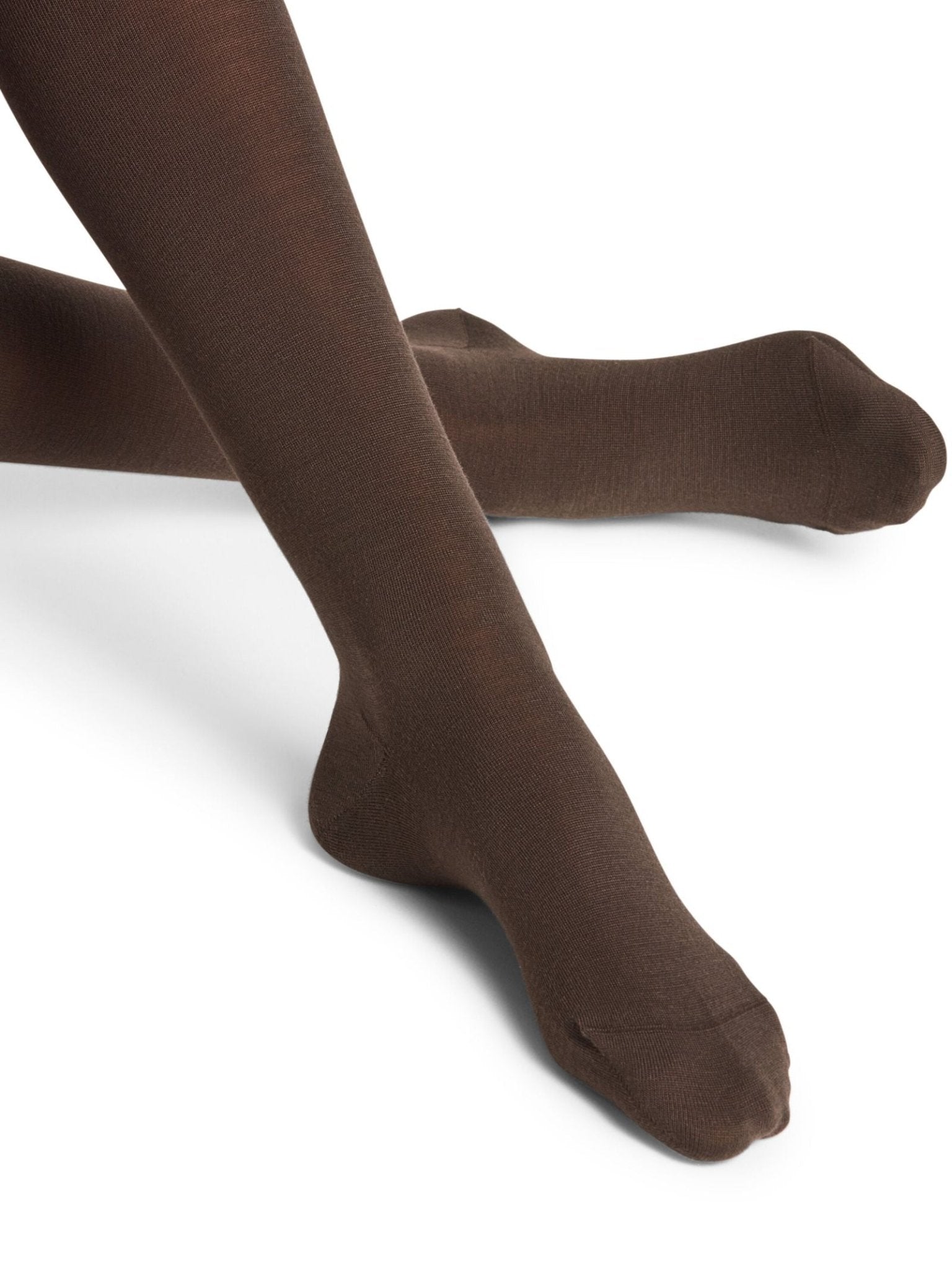 A person models FALKE Merino Tights in opaque brown, crossing their legs and pointing their toes, set against a white background.