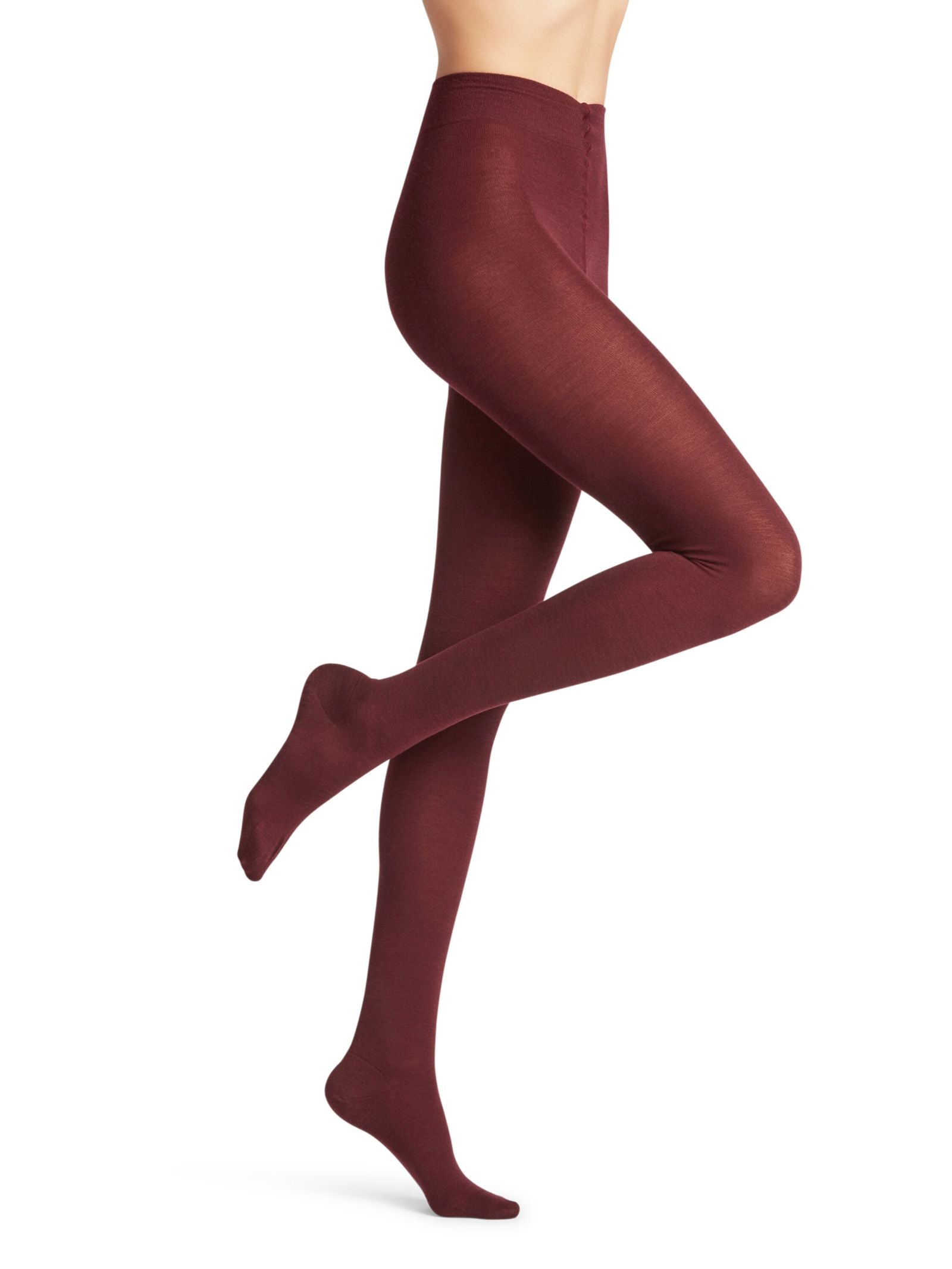 A person models FALKE Merino Tights in burgundy, standing on one leg with the other bent back against a plain white background. The photo highlights the opaque merino wool tights on the lower body, with no shoes visible.