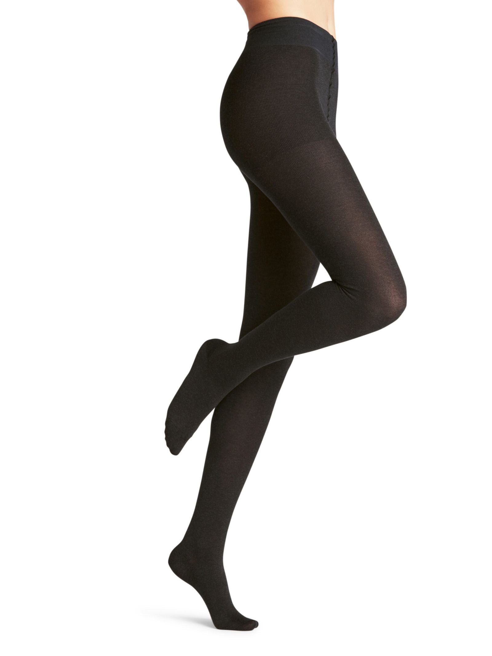A person wearing FALKE Cotton Tights in opaque black stands on one leg, the other bent at the knee, shown from waist to feet against a plain white background. Made with sustainable cotton for superior comfort and style.