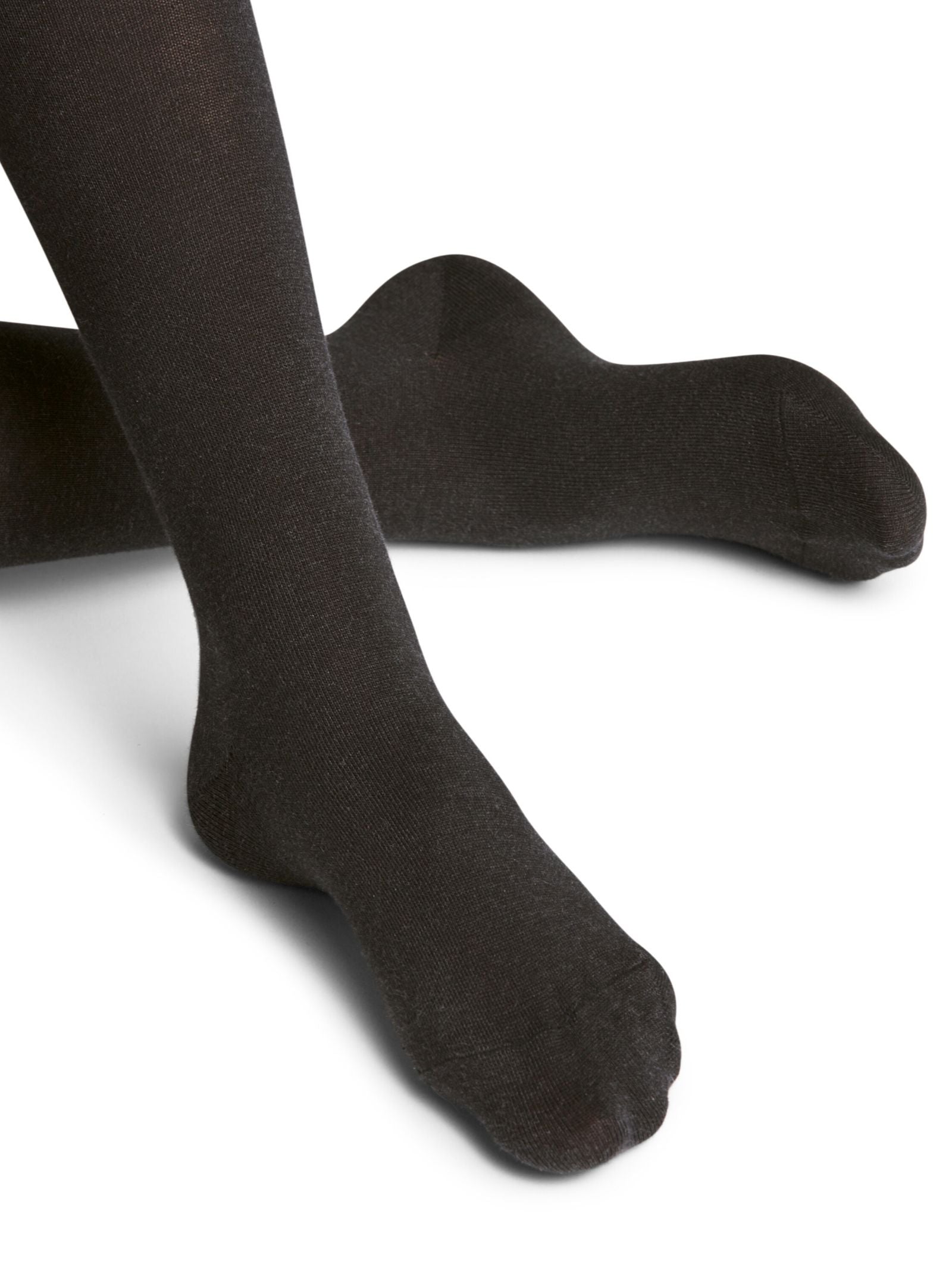 A close-up of two feet in FALKE Cotton Tights, black, with one leg crossed over the other against a plain white background.