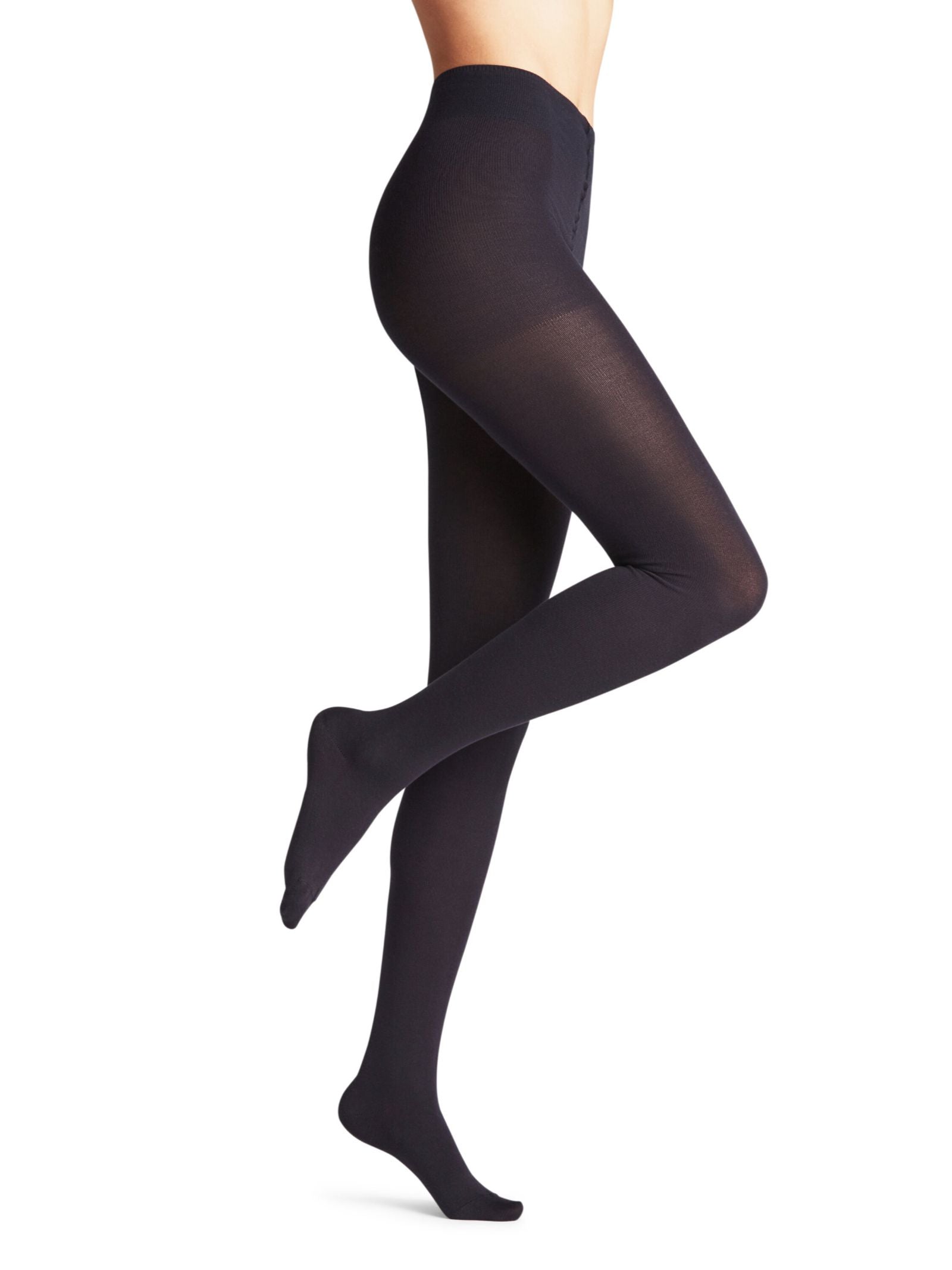 A model showcases FALKE Cotton Tights in opaque black, standing on one leg with the other slightly bent behind, against a plain white background. The image highlights the sustainable tights; upper body is not shown.