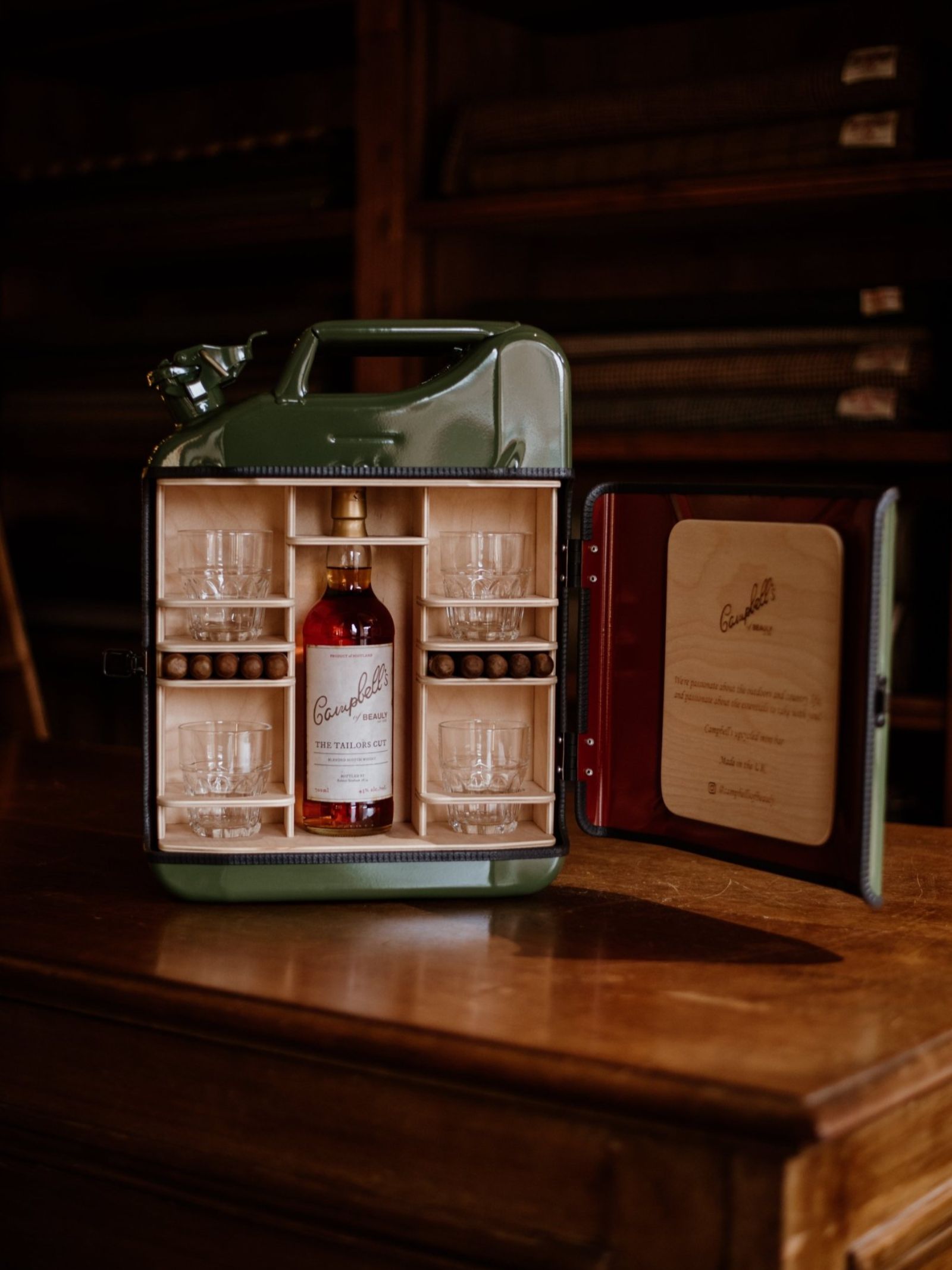 A green jerrycan with its side open reveals a neatly organized mini bar inside, including a bottle of whisky, four glasses, and a compartment of whisky stones, all set within a wooden interior.