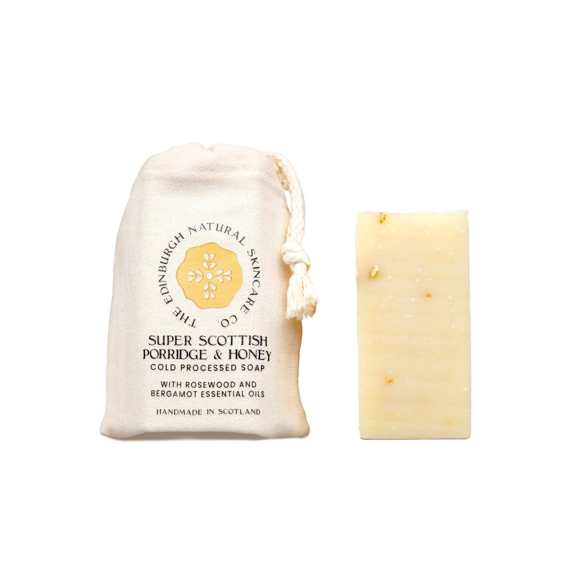A beige fabric pouch labeled "Porridge & Honey Cold Processed Soap" by The Edinburgh Natural Skincare Company stands next to a handmade soap bar with oats, offering natural skincare on a plain white background.