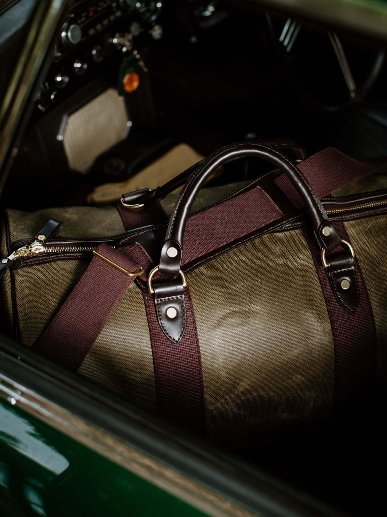 The Campbell's of Beauly Wax Holdall, featuring green waxed canvas, brown leather accents, and bridle leather handles, rests inside a dark car interior.