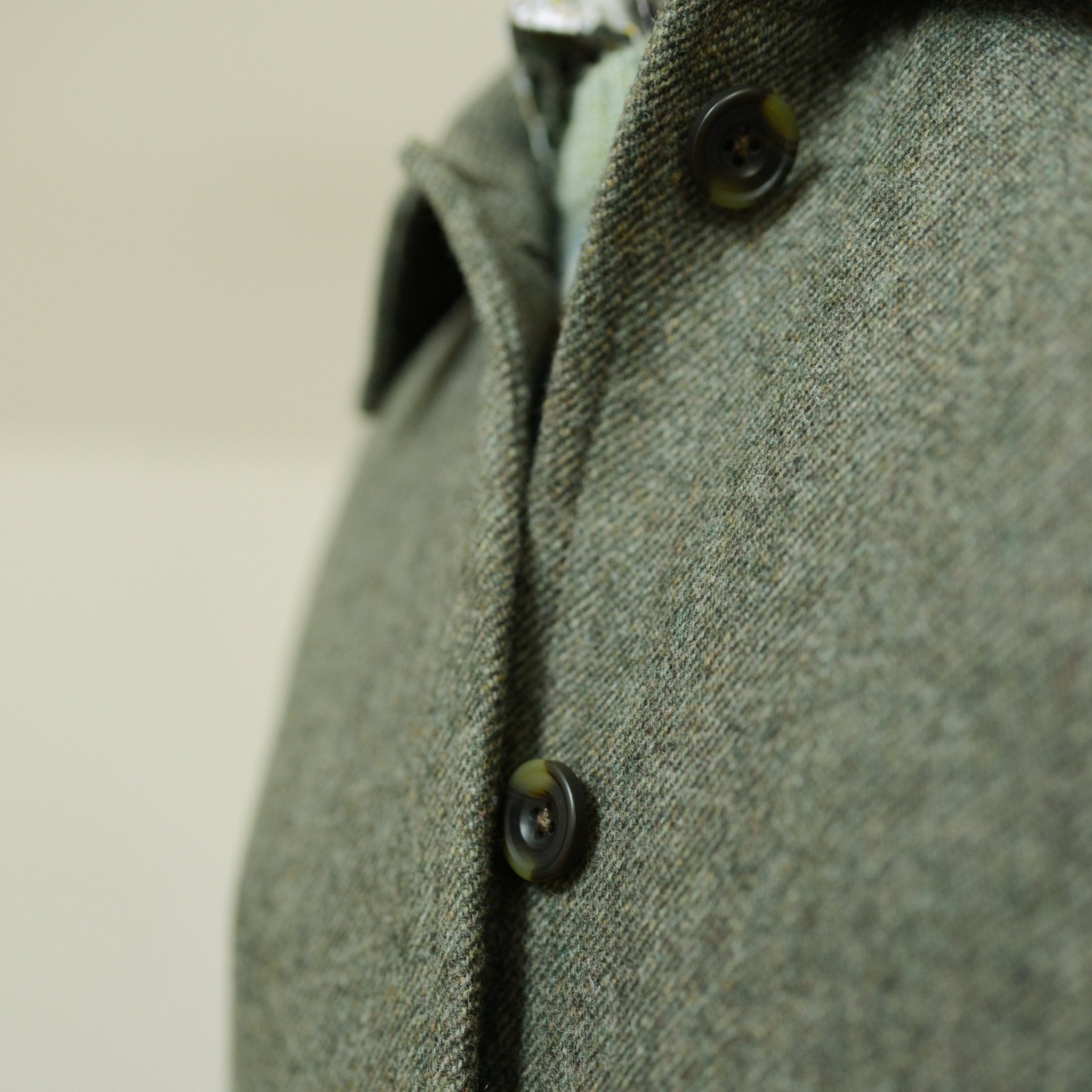 Close-up of the green Auld Stock Heath Collar Coat by Campbell's of Beauly, perfect for everyday wear. Features two black buttons and a textured collar, with sharp detail on the fabric against a blurred background.