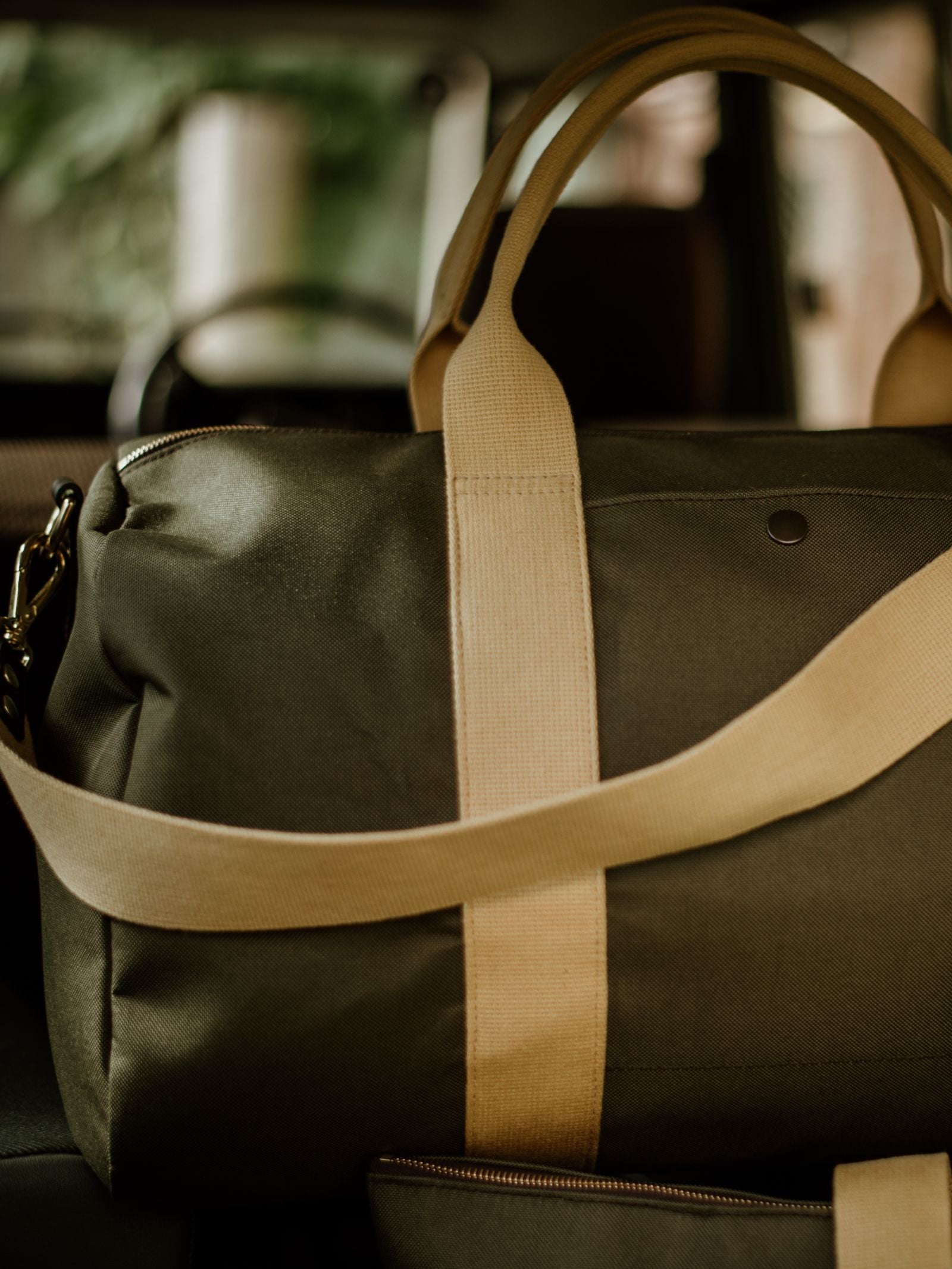 The Campbell's of Beauly Utility Medium Duffle, made from heavy-duty canvas with beige straps, rests inside a vehicle. Its dark green color stands out against the blurred background visible through the window.